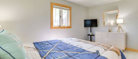 A bedroom with a bed, a television, a dresser, and a window.