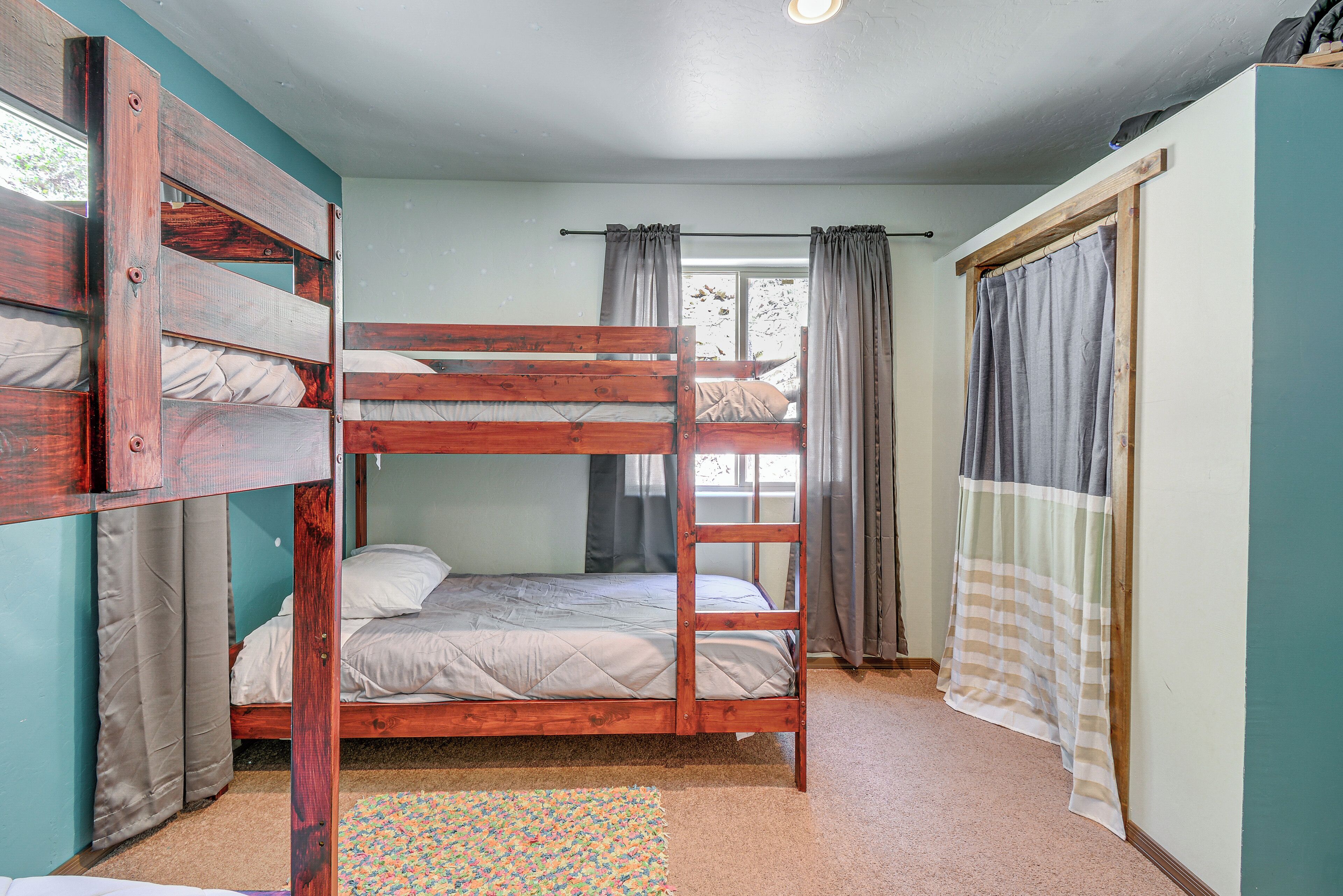 A bunk bed room with a window, curtains, and a patterned rug.