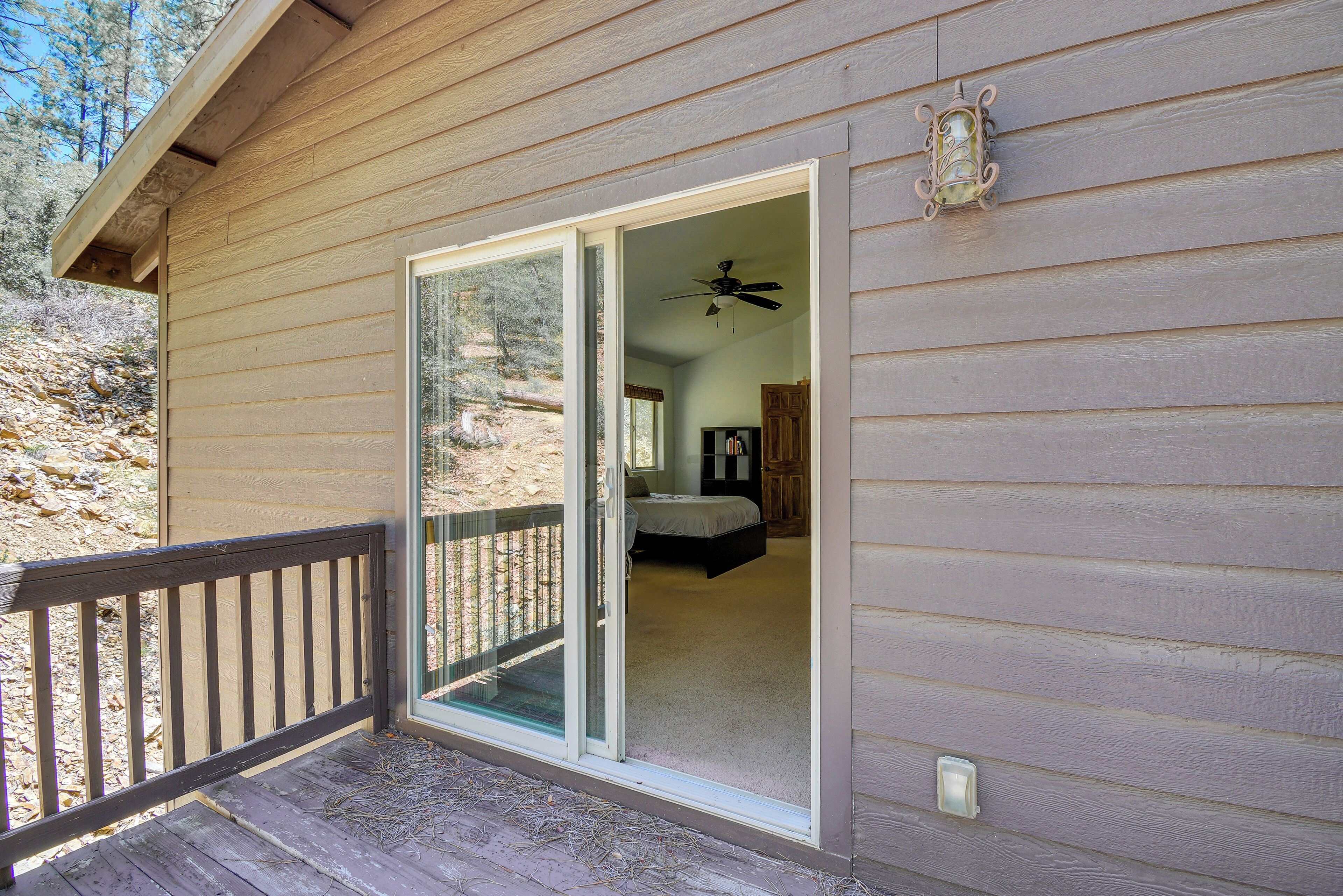A wooden cabin with a sliding glass door leading to a bedroom with a bed and a ceiling fan.
