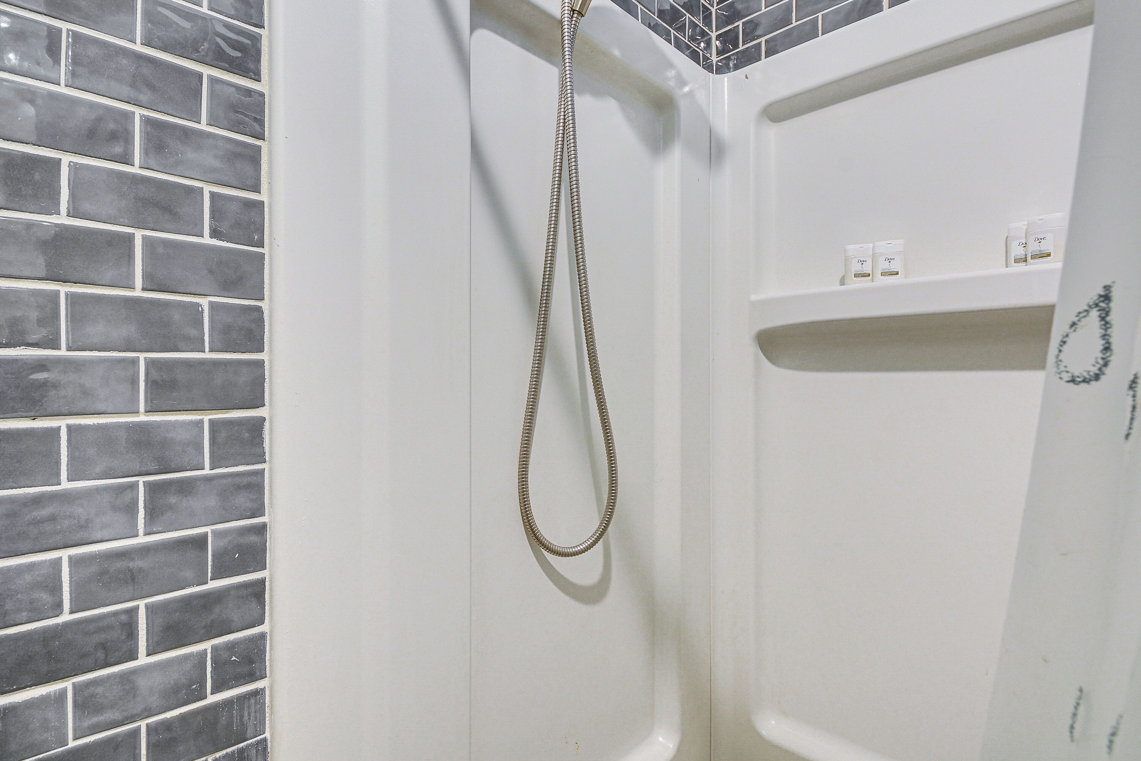 Area doccia con soffione, parete rivestita in piastrelle ed uno scaffale con articoli da bagno.