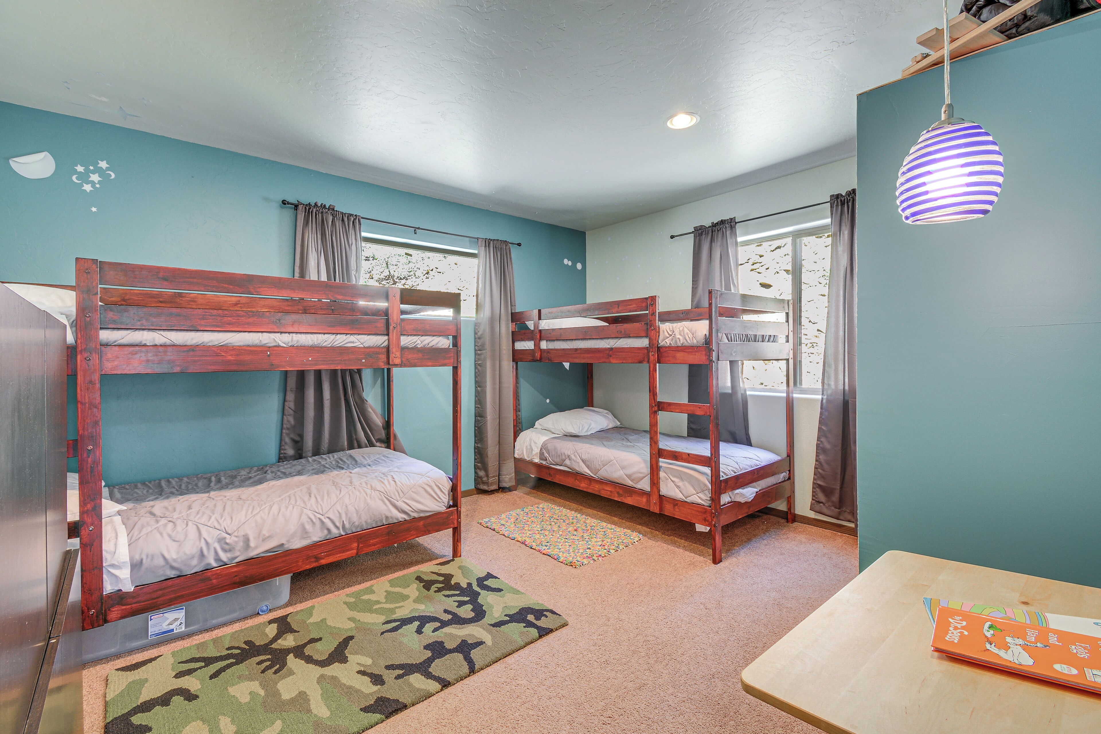 A room with bunk beds, a small table, and a window with curtains.