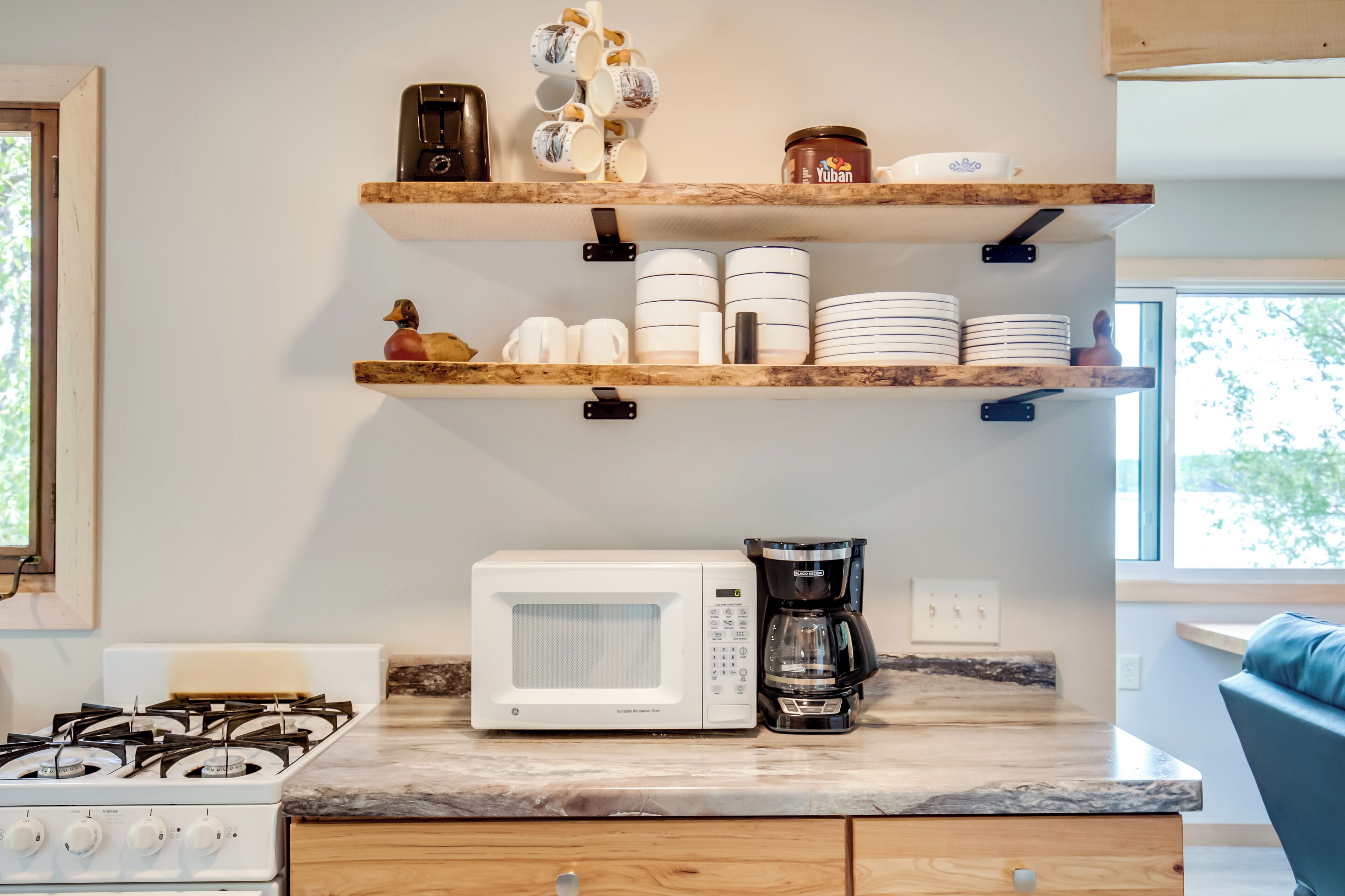 Een keuken met een witte magnetron, een koffiezetapparaat en houten planken met servies en mokken.