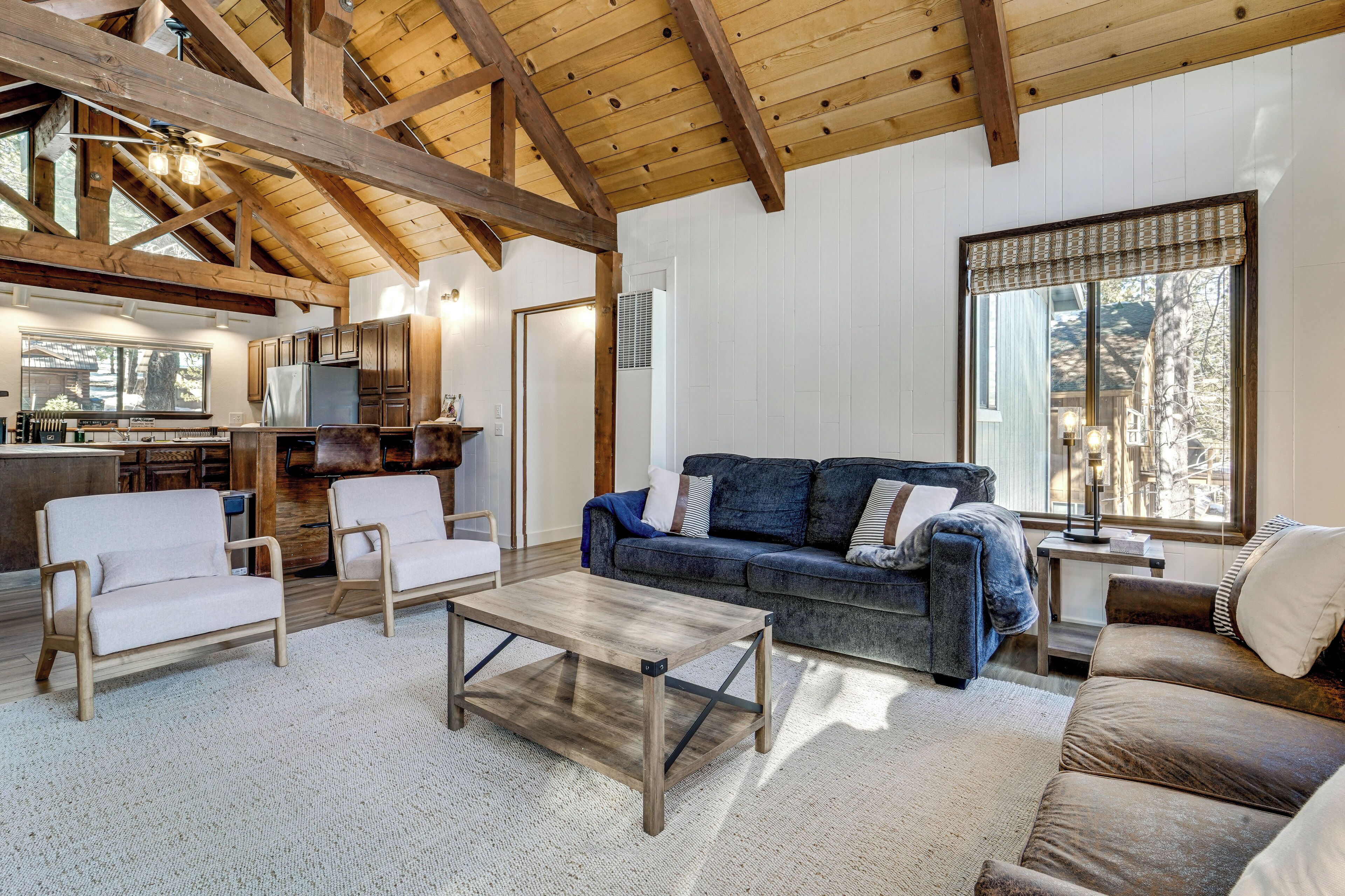 A spacious living area with a wooden ceiling, a large window, and a cozy seating arrangement including a sofa and chairs.