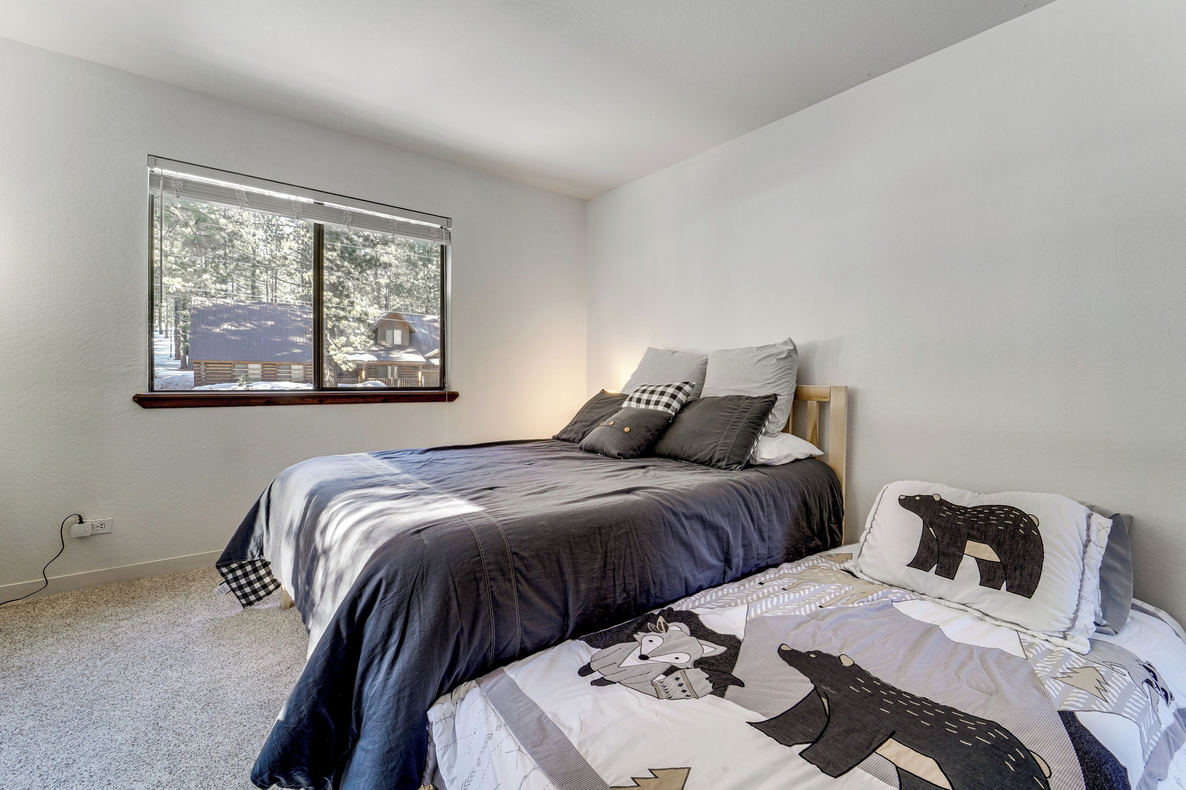 A bedroom with a large window, a bed with a patterned bedspread, and a view of a cabin outside.
