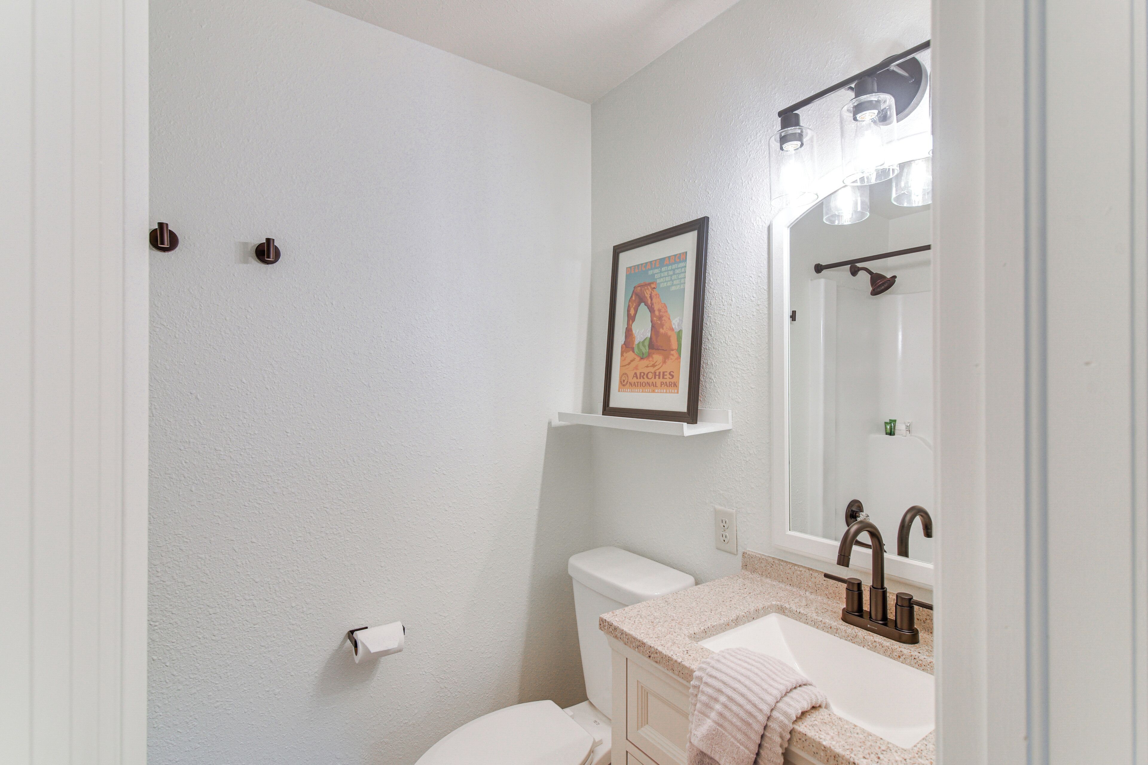 Une salle de bain avec des toilettes, un lavabo et un miroir. Un tableau encadré est accroché au mur, au-dessus du lavabo.