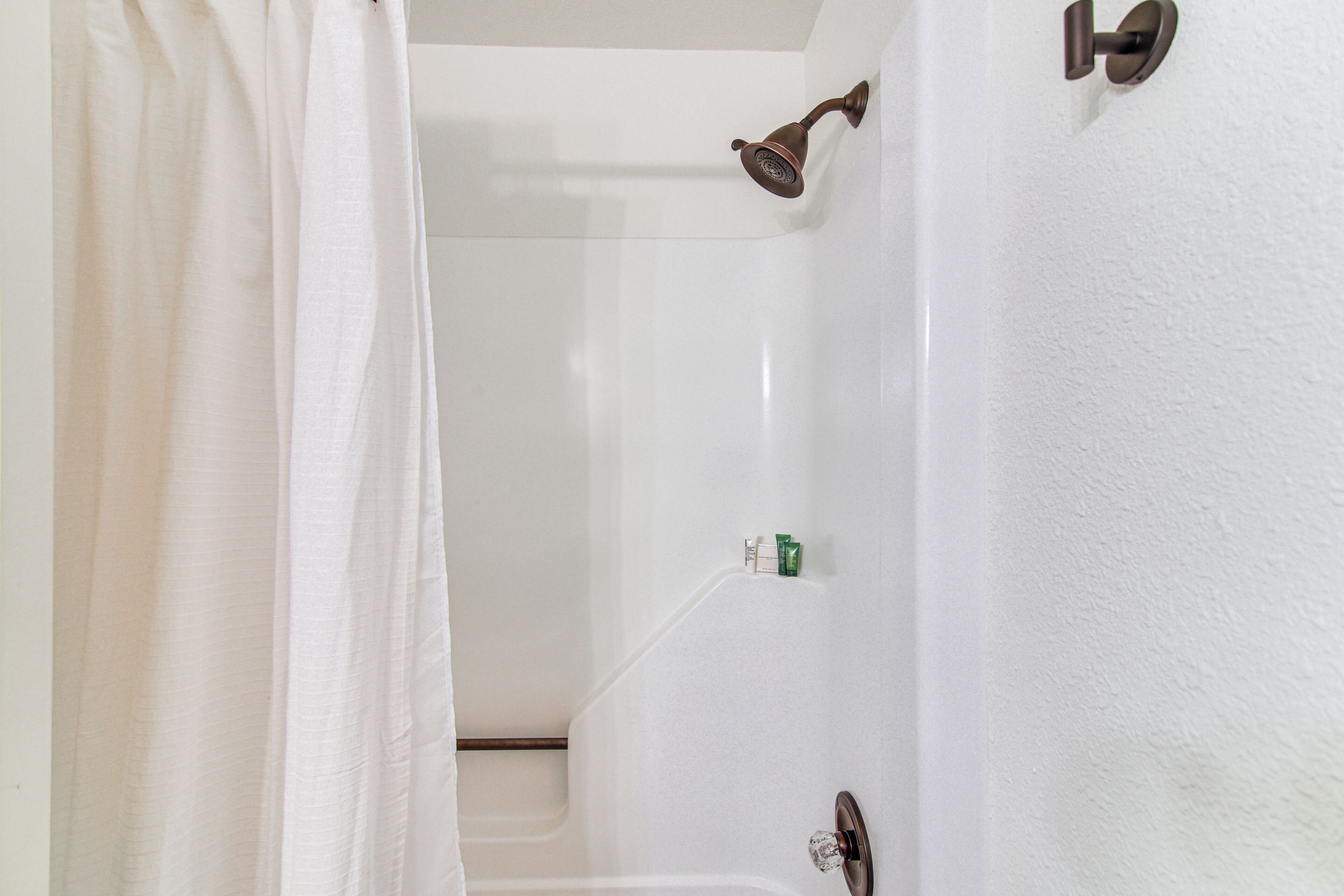 A bathroom with a shower, a white bathtub, and a door with a round handle.