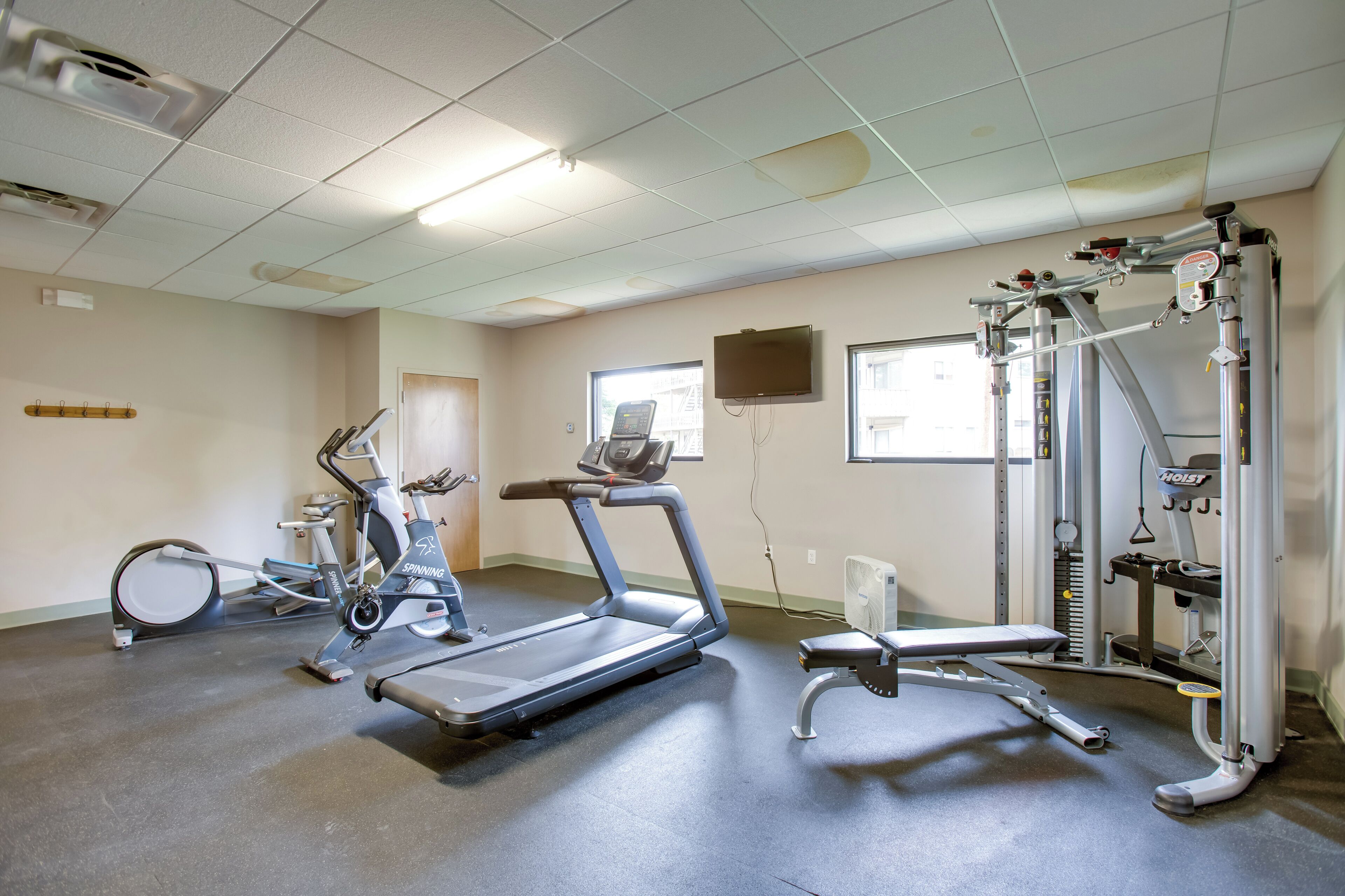 Ein Fitnessstudio mit Laufbändern, Krafttrainingsgeräten und einem Fernseher an der Wand.