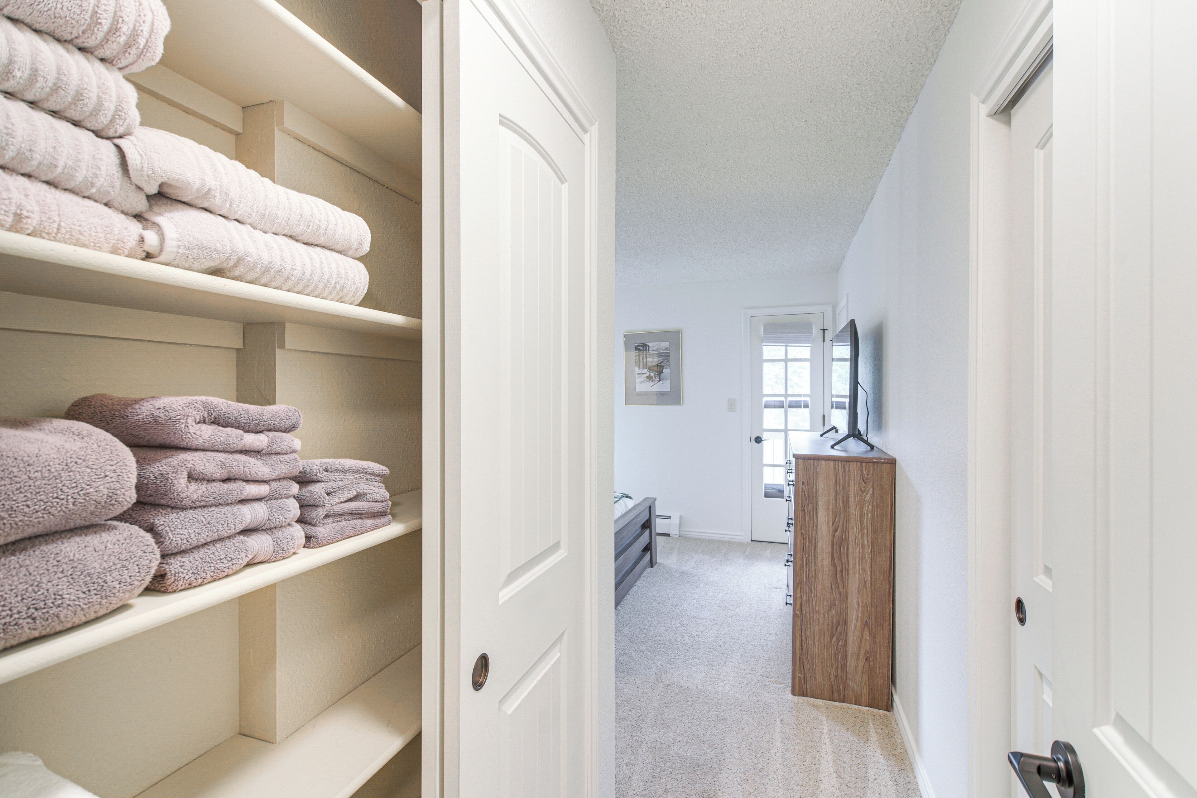 Quarto de hotel com um guarda-roupa bem organizado, uma cômoda de madeira e uma cama ao fundo.