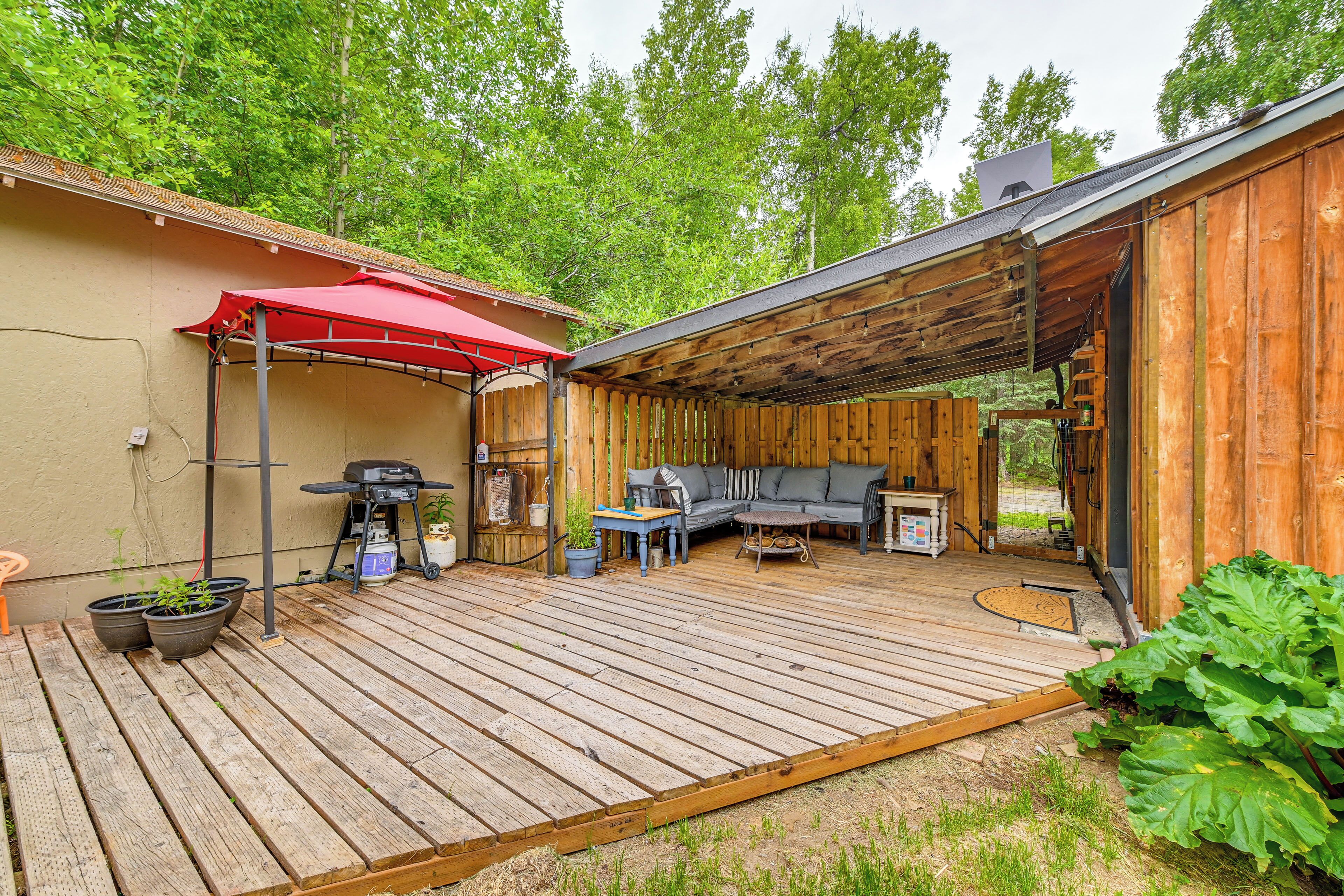 A wooden deck with outdoor furniture, a barbecue grill, and a red umbrella.
