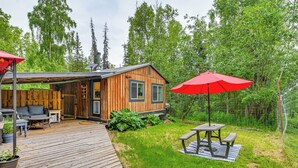 Una cabaña de madera con terraza, mobiliario exterior y una mesa de picnic.