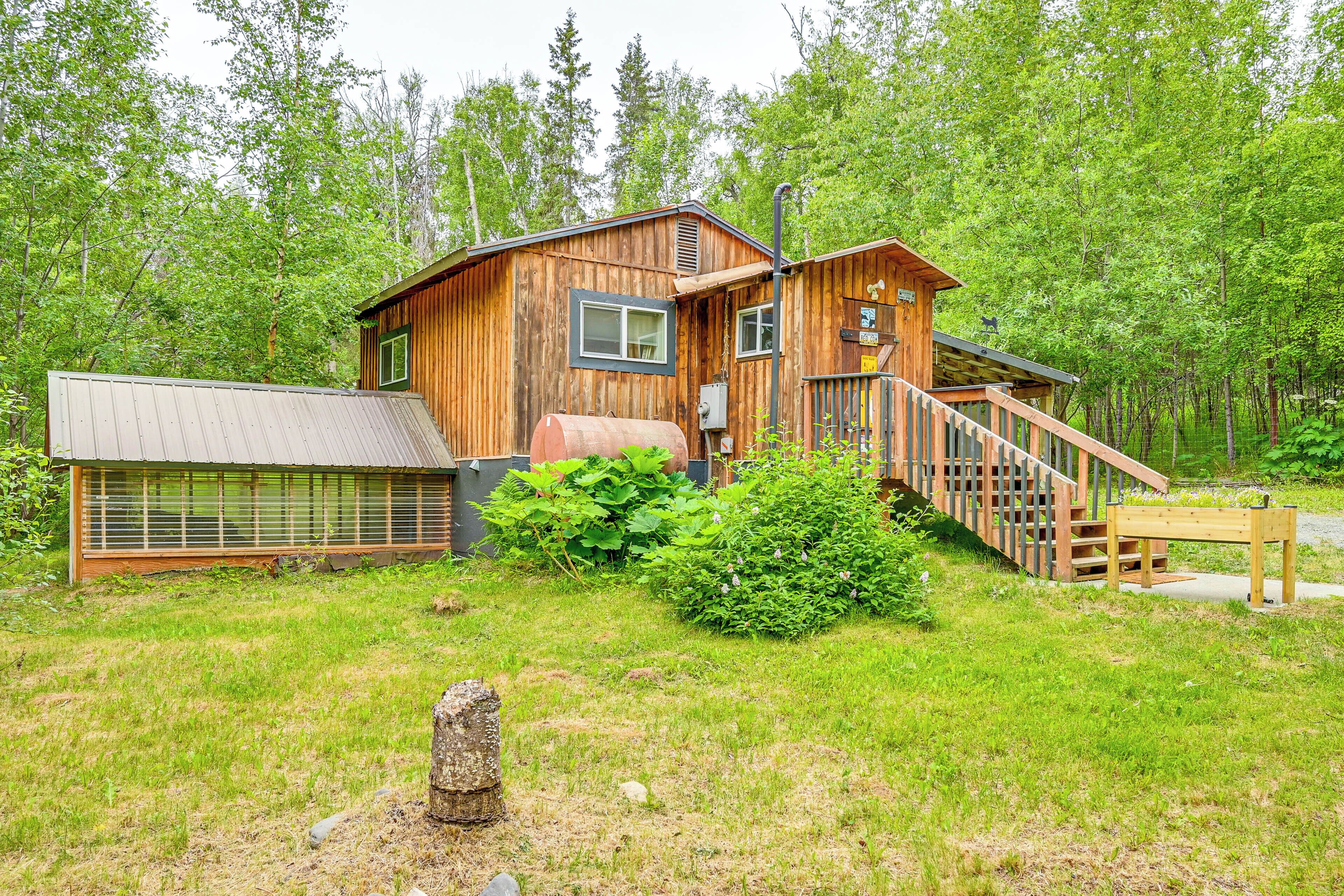 A wooden cabin with a metal roof, a wooden deck, and a staircase leading to a porch.