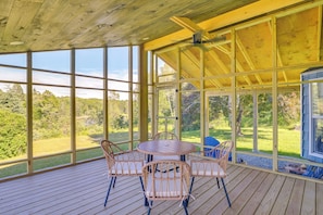 Une terrasse extérieure couverte, dotée d’un plancher en bois et de grandes fenêtres, qui offre une vue sur un paysage verdoyant.