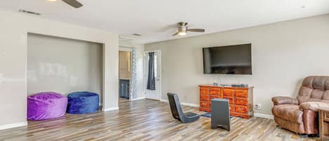 A spacious living area with hardwood flooring, a ceiling fan, a leather recliner, a flat-screen TV, and a wooden cabinet.
