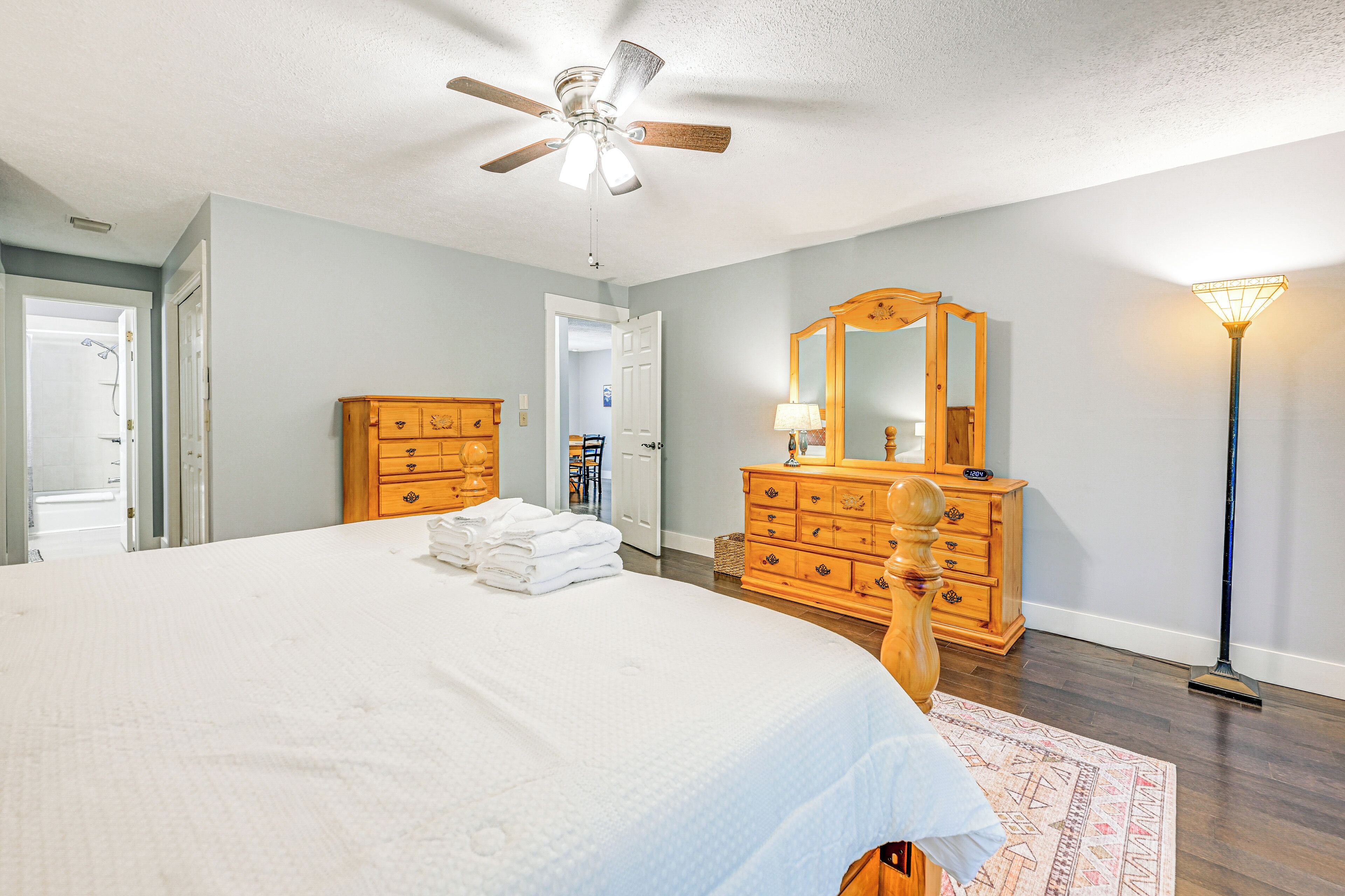 A bedroom with a large bed, wooden dresser, and a ceiling fan.