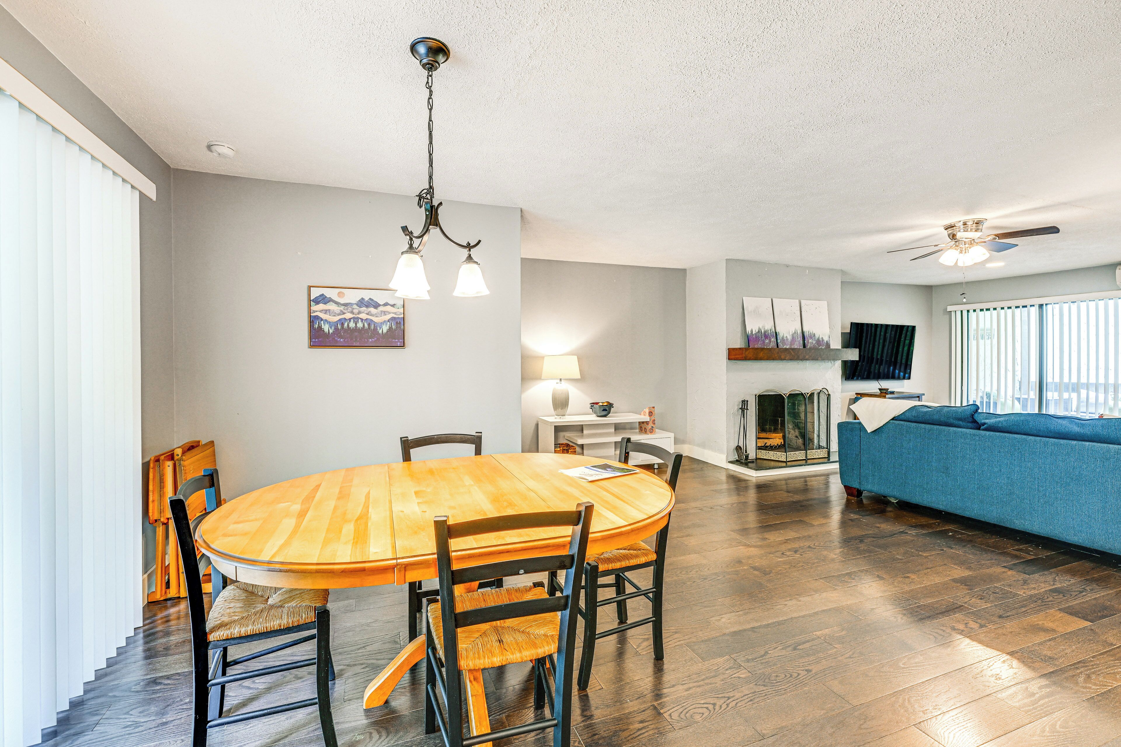 A dining area with a wooden table and chairs, a ceiling fan, and a sofa in a living room with hardwood floors.
