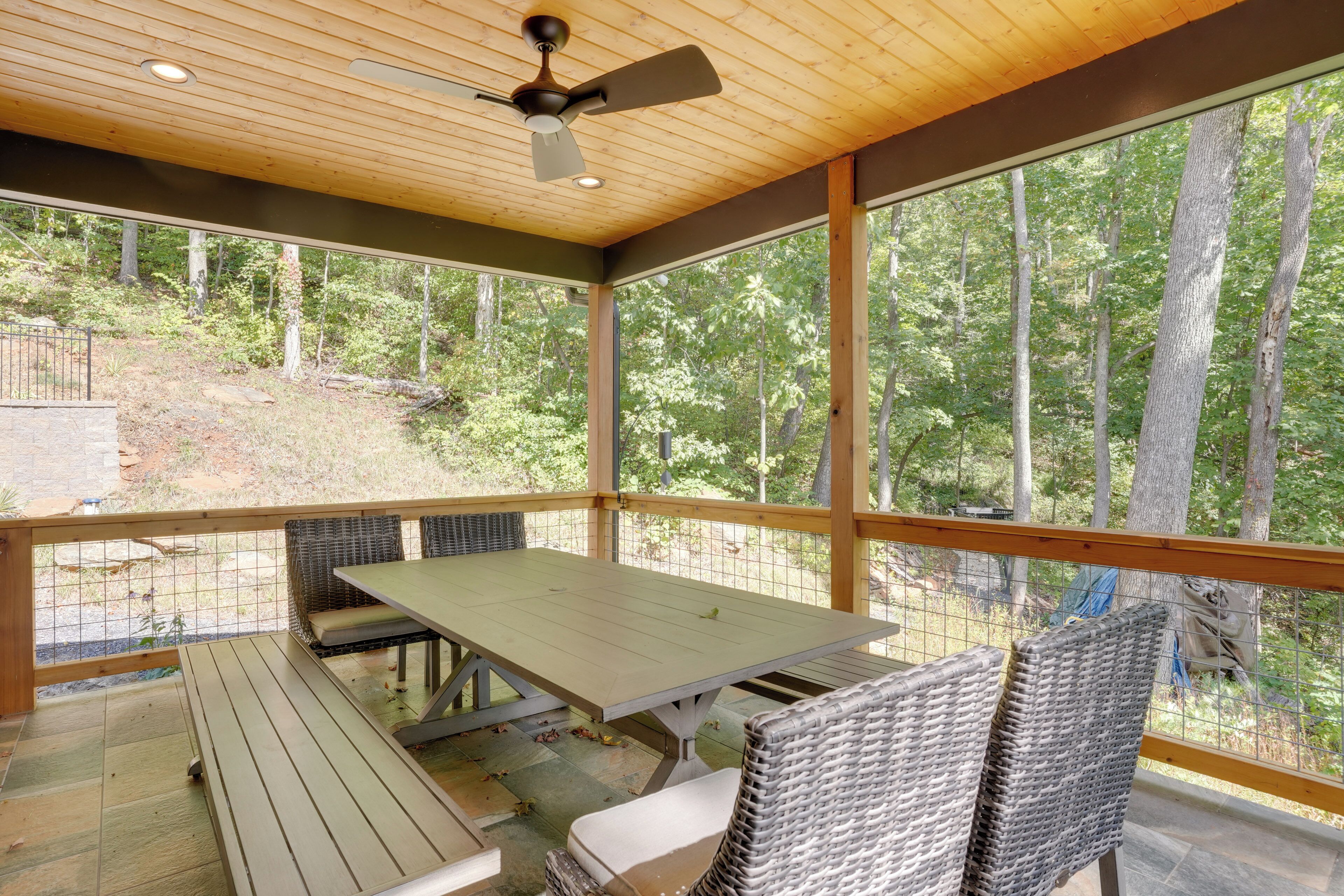 A covered outdoor patio with a table and chairs, large windows, and a ceiling fan.