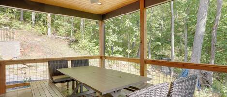 A covered outdoor patio with a table and chairs, large windows, and a ceiling fan.