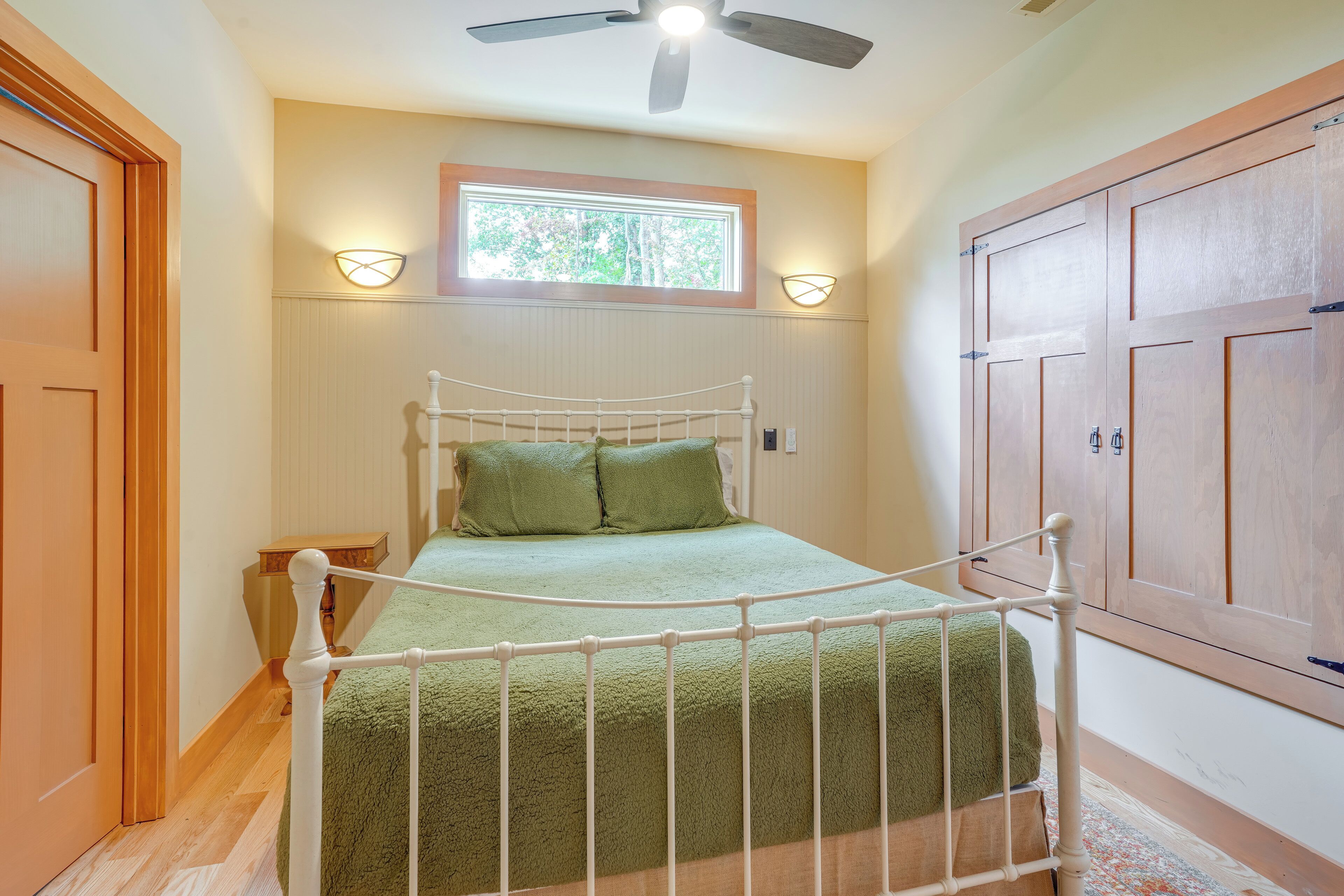 A bedroom with a bed, a window, a ceiling fan, and wooden doors.