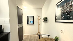 Un pasillo estrecho con una mesa de comedor de madera, sillas, una vela y un cuadro en la pared.