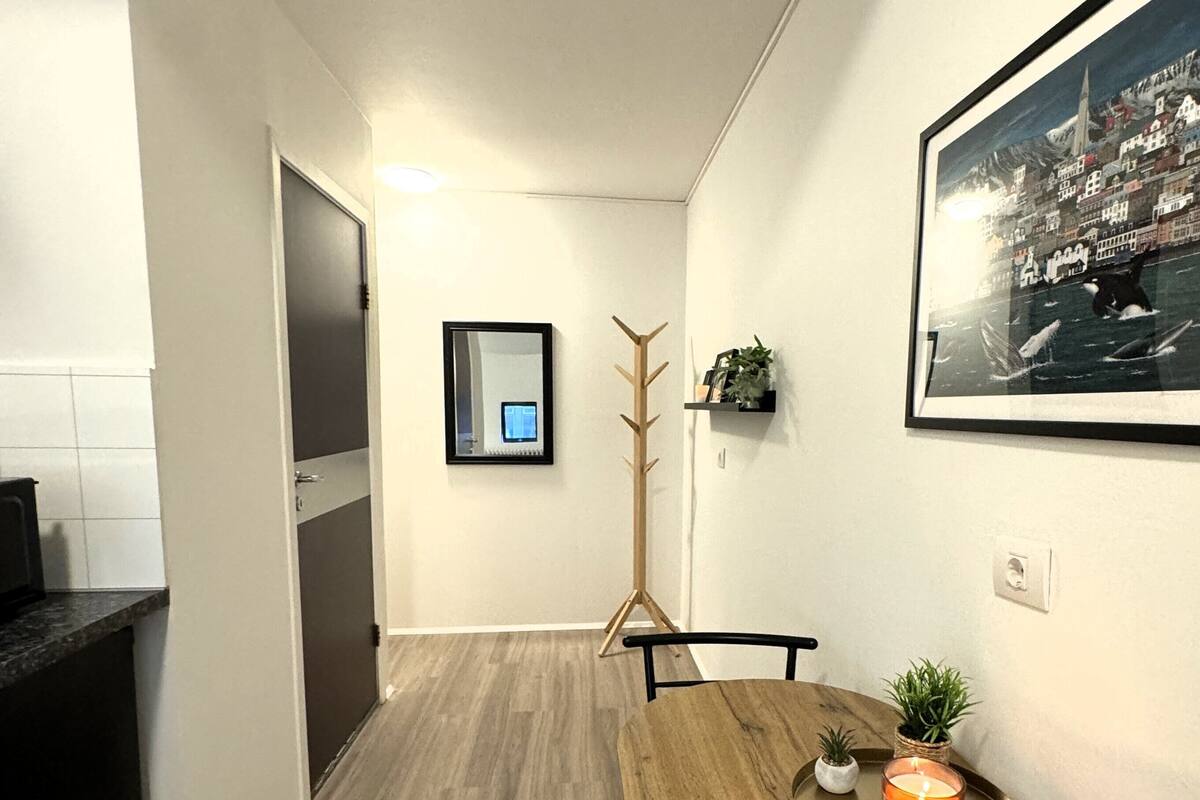Un pasillo estrecho con una mesa de comedor de madera, sillas, una vela y un cuadro en la pared.