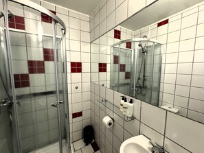Une salle de bain moderne avec une douche à l’italienne en verre, un lavabo blanc et un miroir au-dessus.