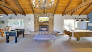 A spacious living area with a foosball table, a pool table, and a stone fireplace.