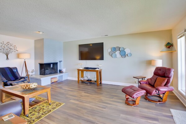 A living room with a fireplace, a television, a leather chair, and a coffee table. - Comfortable Lincoln City Condo w/ Patio & Views! (Gleneden Beach)