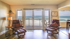 A room with two leather recliners facing a sliding glass door leading to a balcony with a view of the ocean.