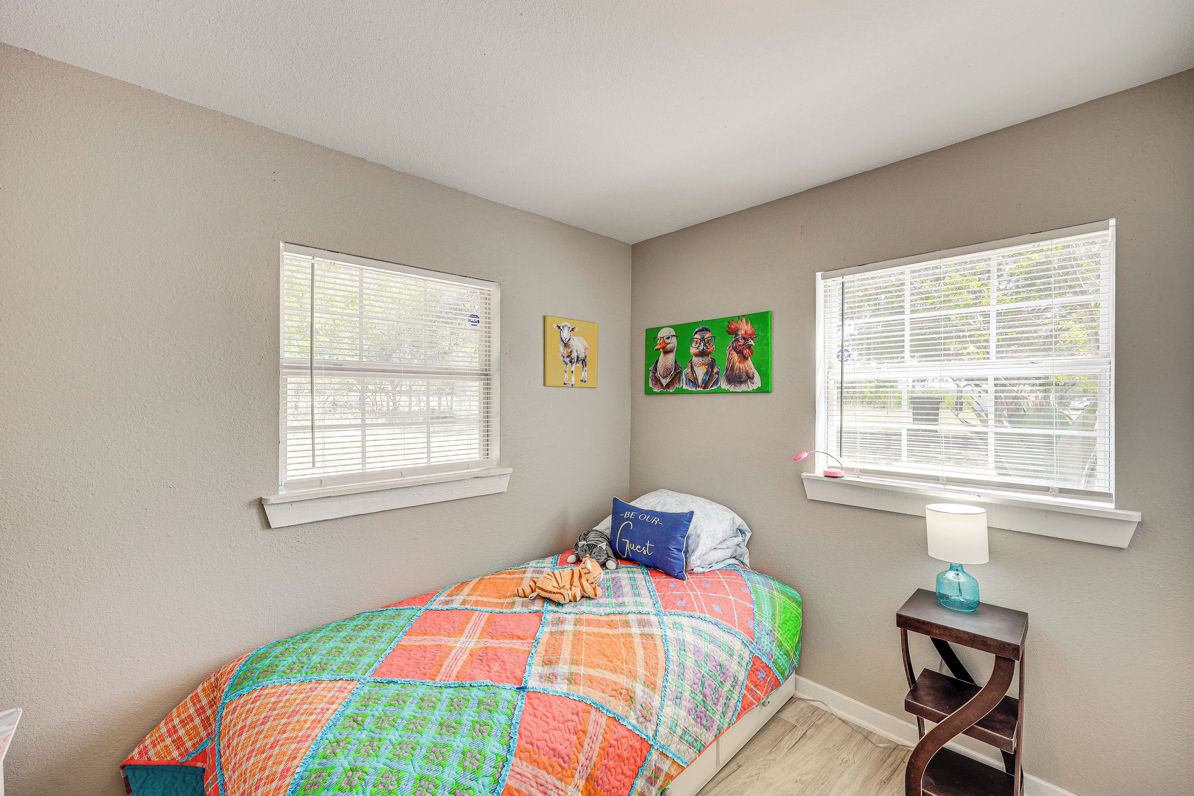 A bedroom with a bed, two windows, a nightstand, and wall art.