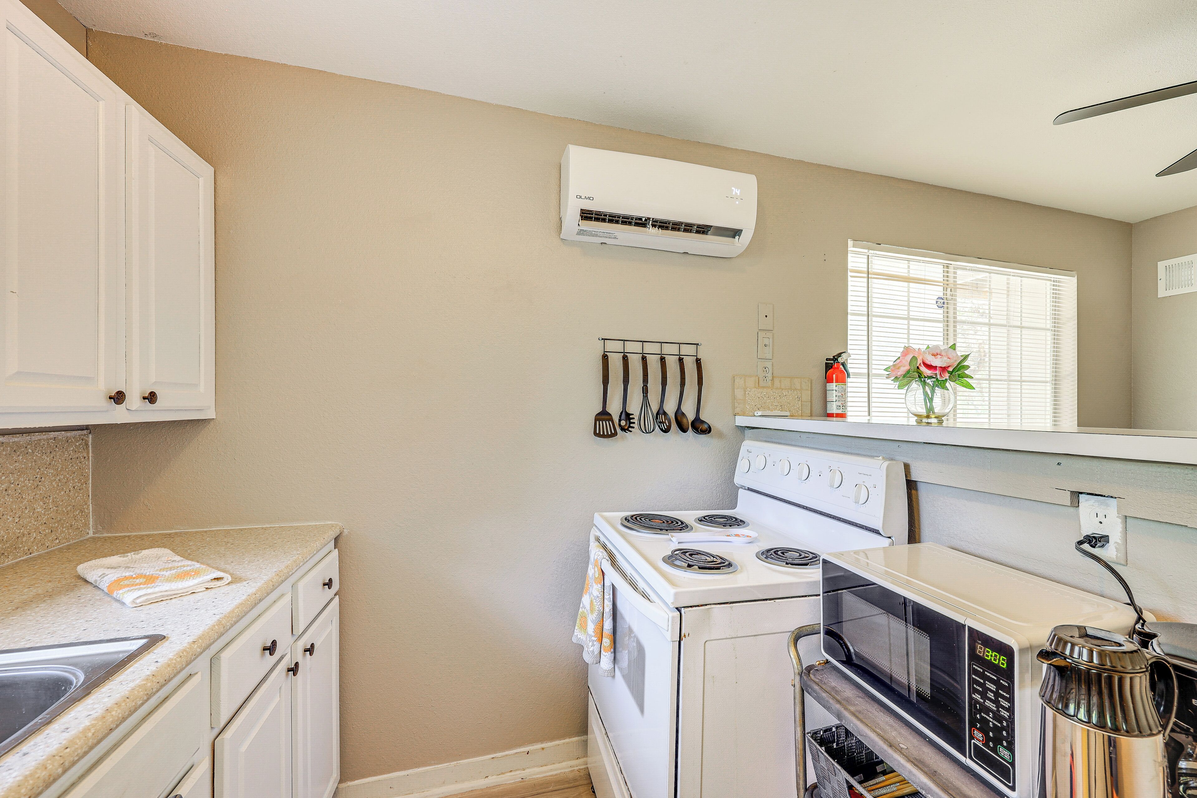 A compact kitchen with a stove, microwave, and oven, white cabinets, and an air conditioning unit.