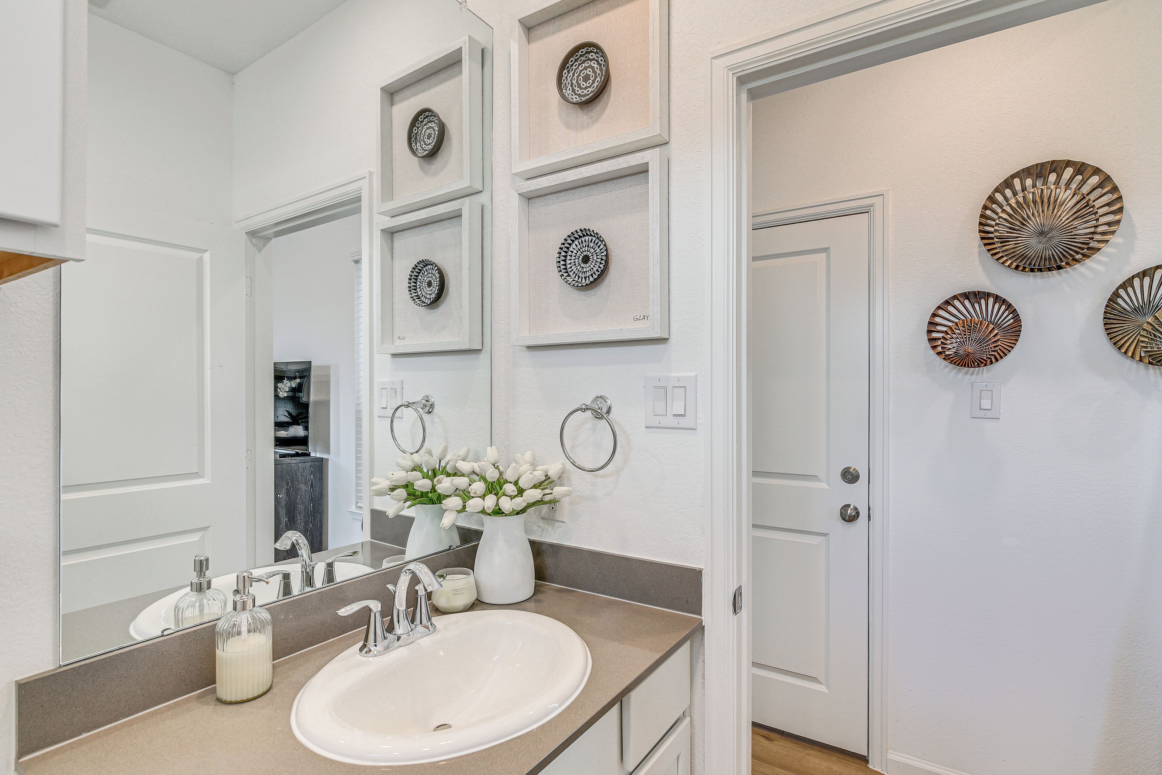 A bathroom with a white sink, mirror, and decorative plates on the wall.