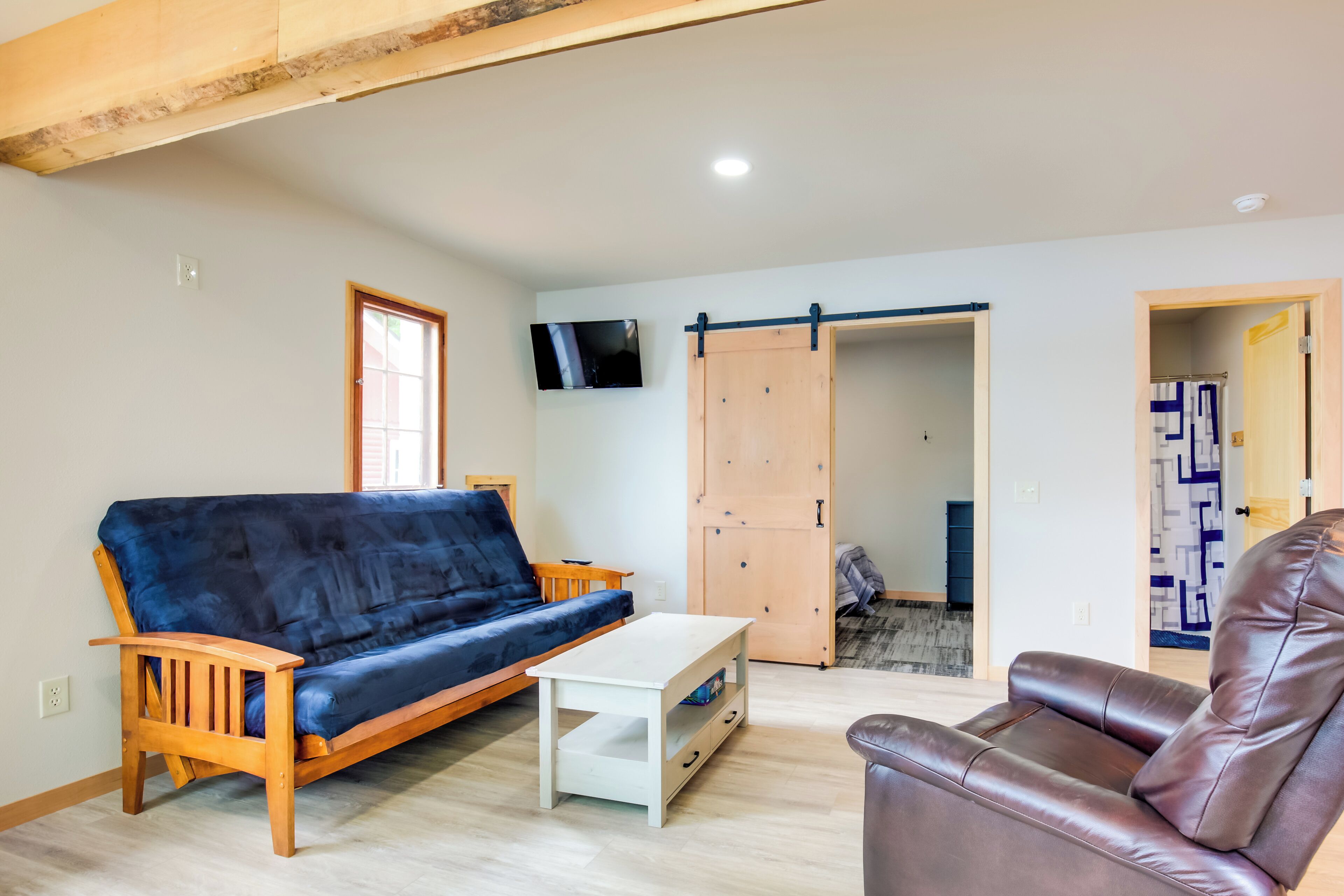 A living room with a blue sofa, a white coffee table, a brown leather chair, a wooden cabinet, and a sliding door leading to another room.