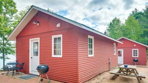 Eine rote Holzhütte mit Tür, Fenstern, einem Grill, einem Picknicktisch und einer kleinen Sitzgruppe im Freien.