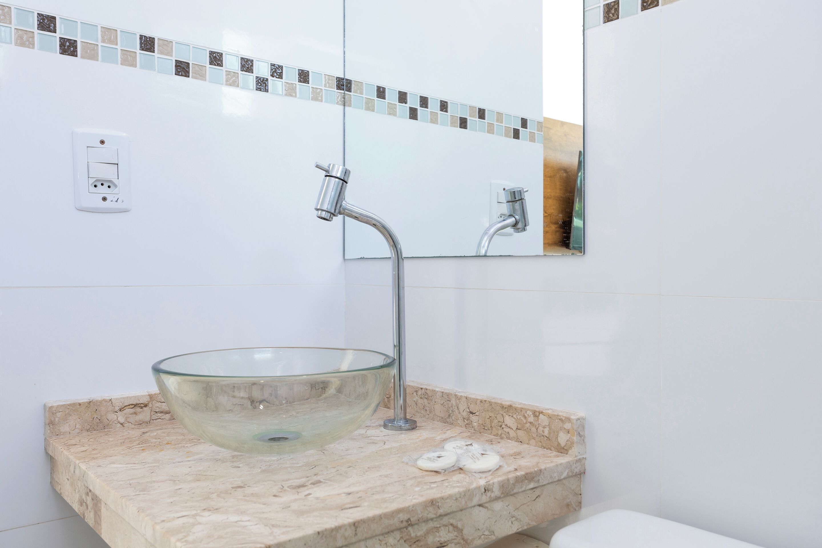 A bathroom with a glass bowl sink, a mirror, and a tiled backsplash.