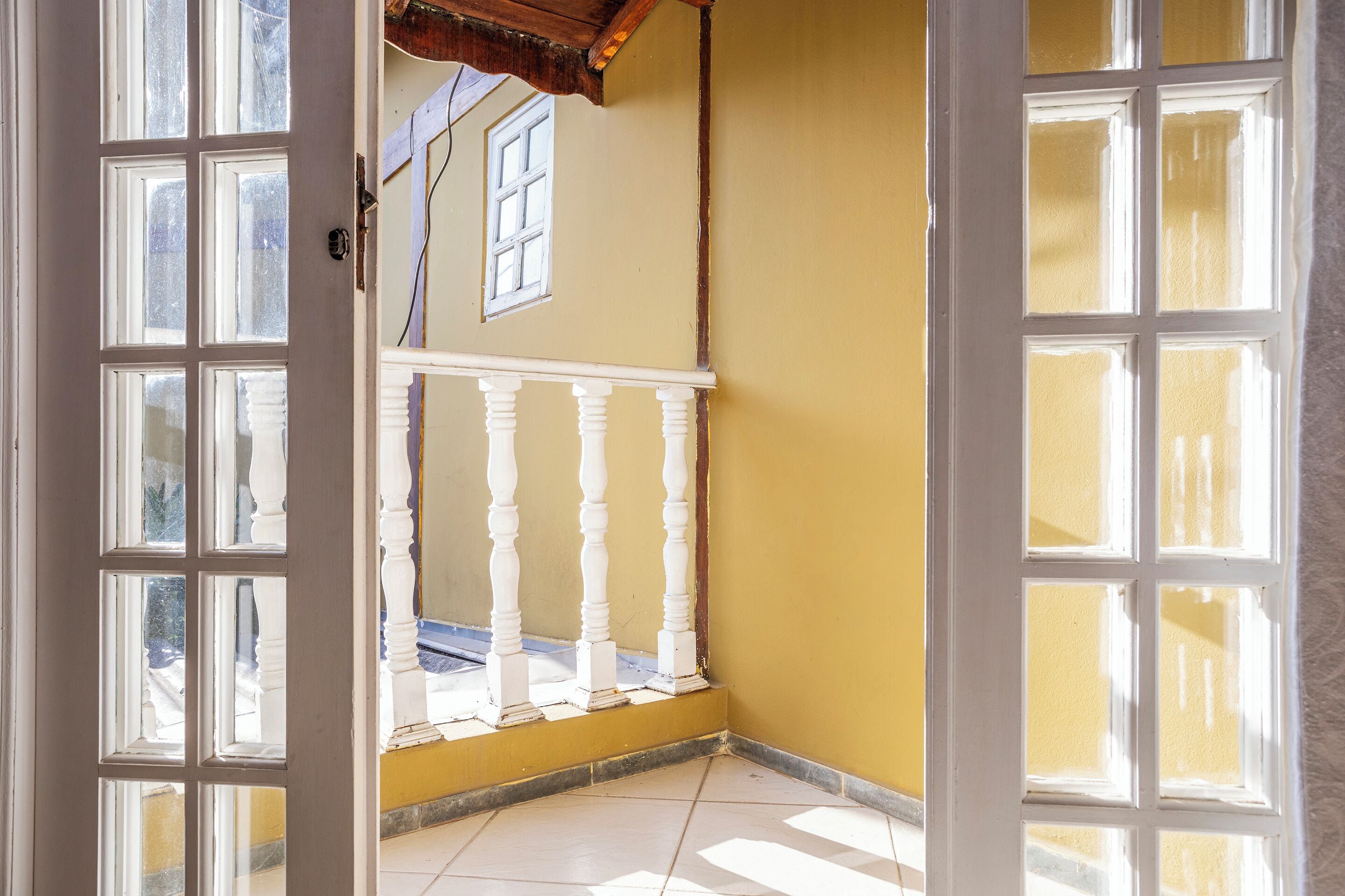 An open door leading to a balcony with a white balustrade, a yellow wall, and a tiled floor.