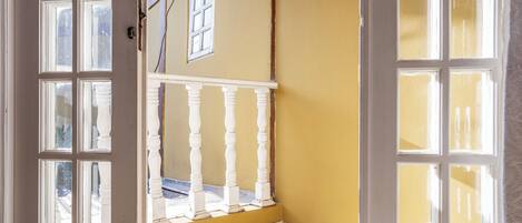 An open door leading to a balcony with a white balustrade, a yellow wall, and a tiled floor.