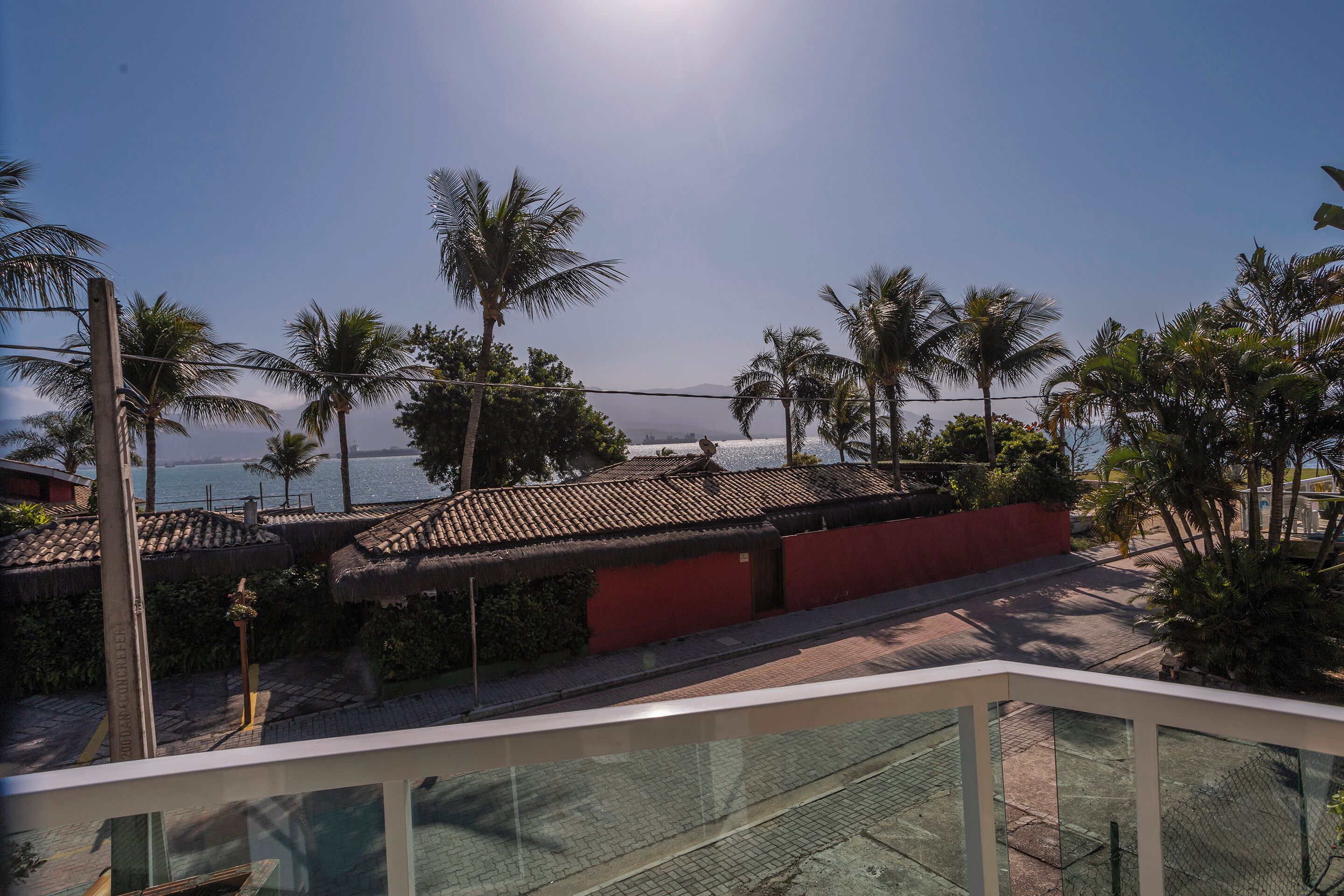 A coastal view with palm trees, a red building, and a clear sky.