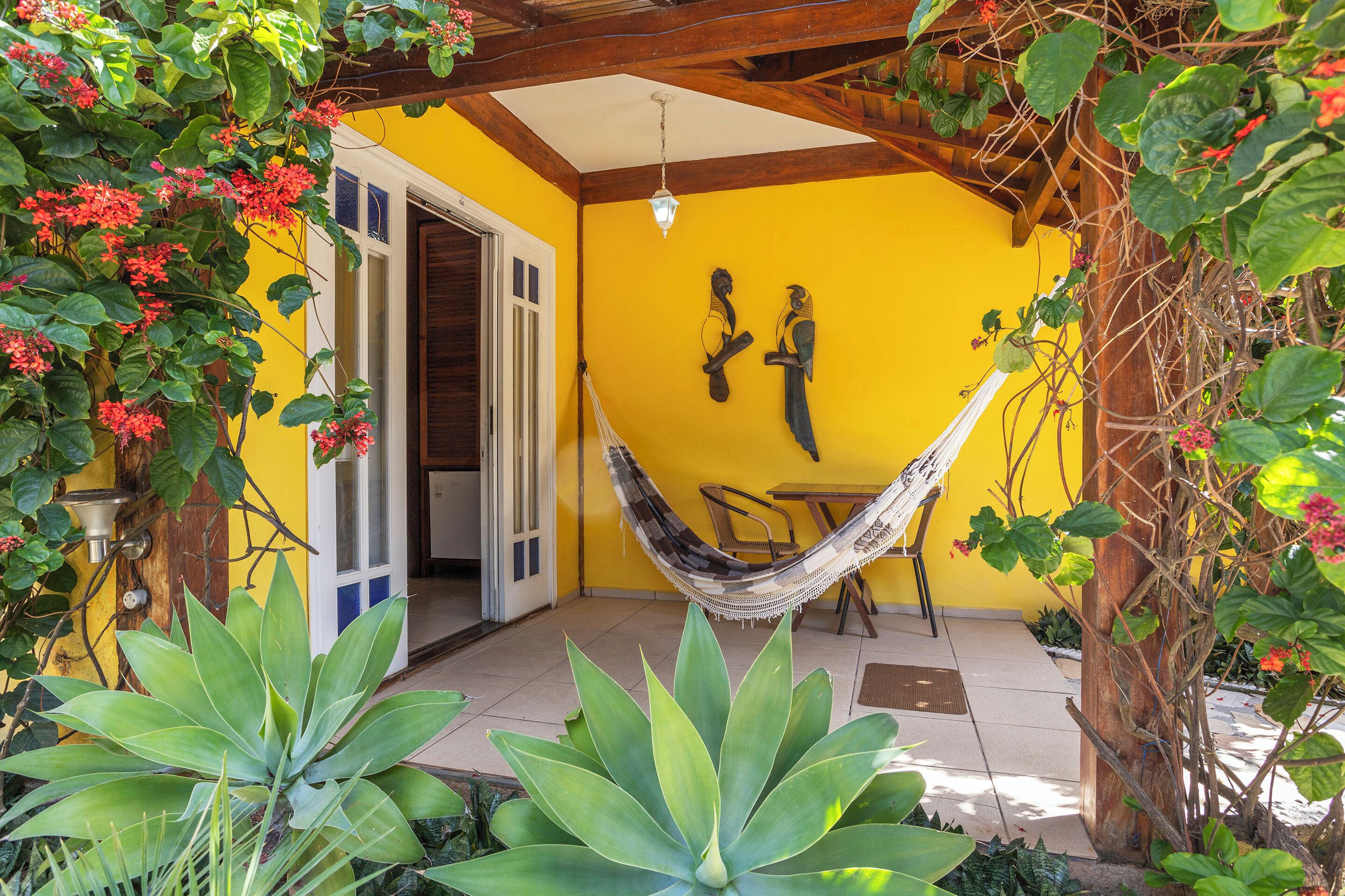 Habitación con paredes amarillas, una hamaca, techo de madera y una puerta que da al exterior.