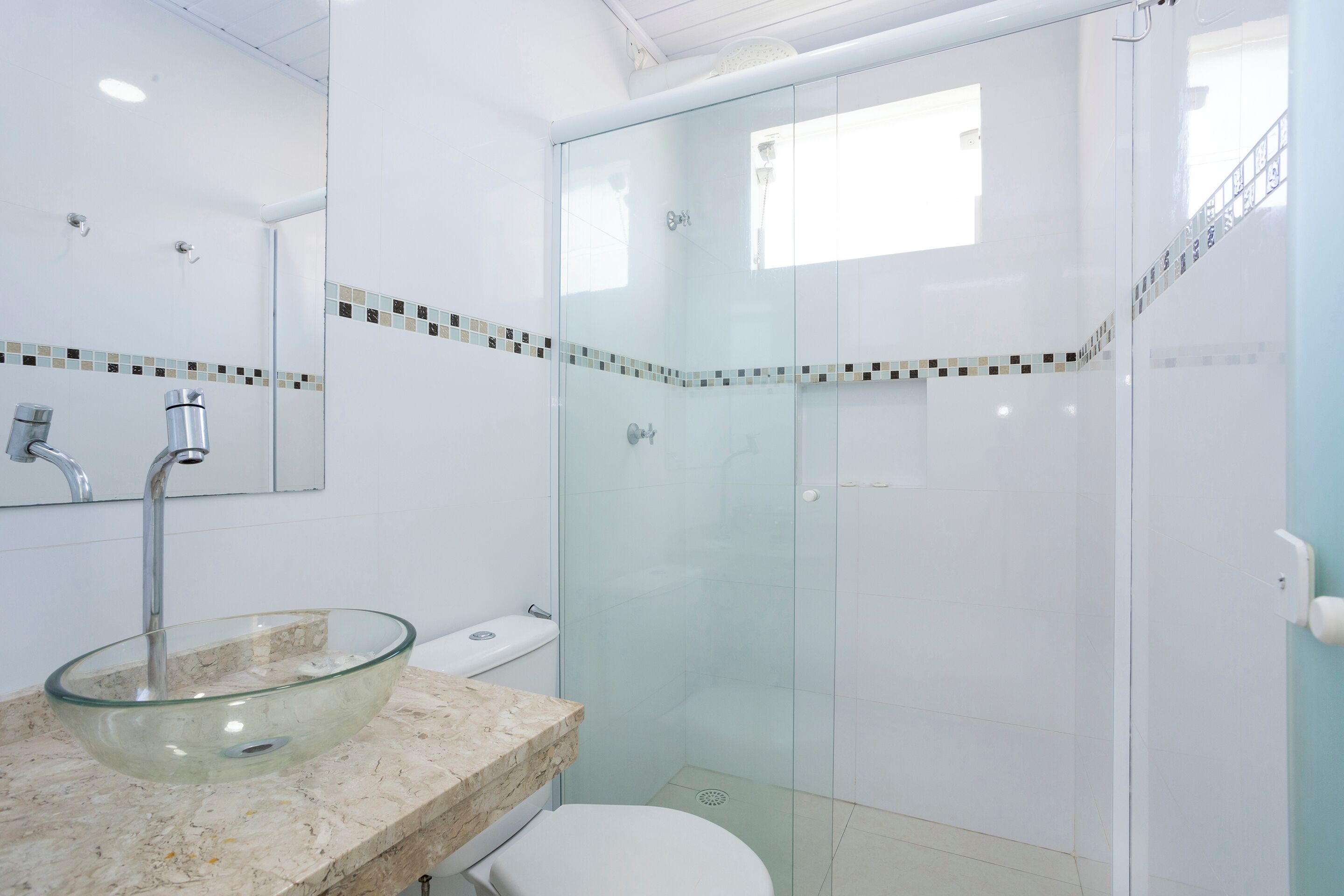 A modern bathroom with a glass-enclosed shower, a glass sink, and a toilet.