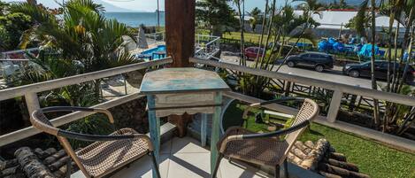 A balcony with a table and chairs, overlooking a pool and a parking area with cars.