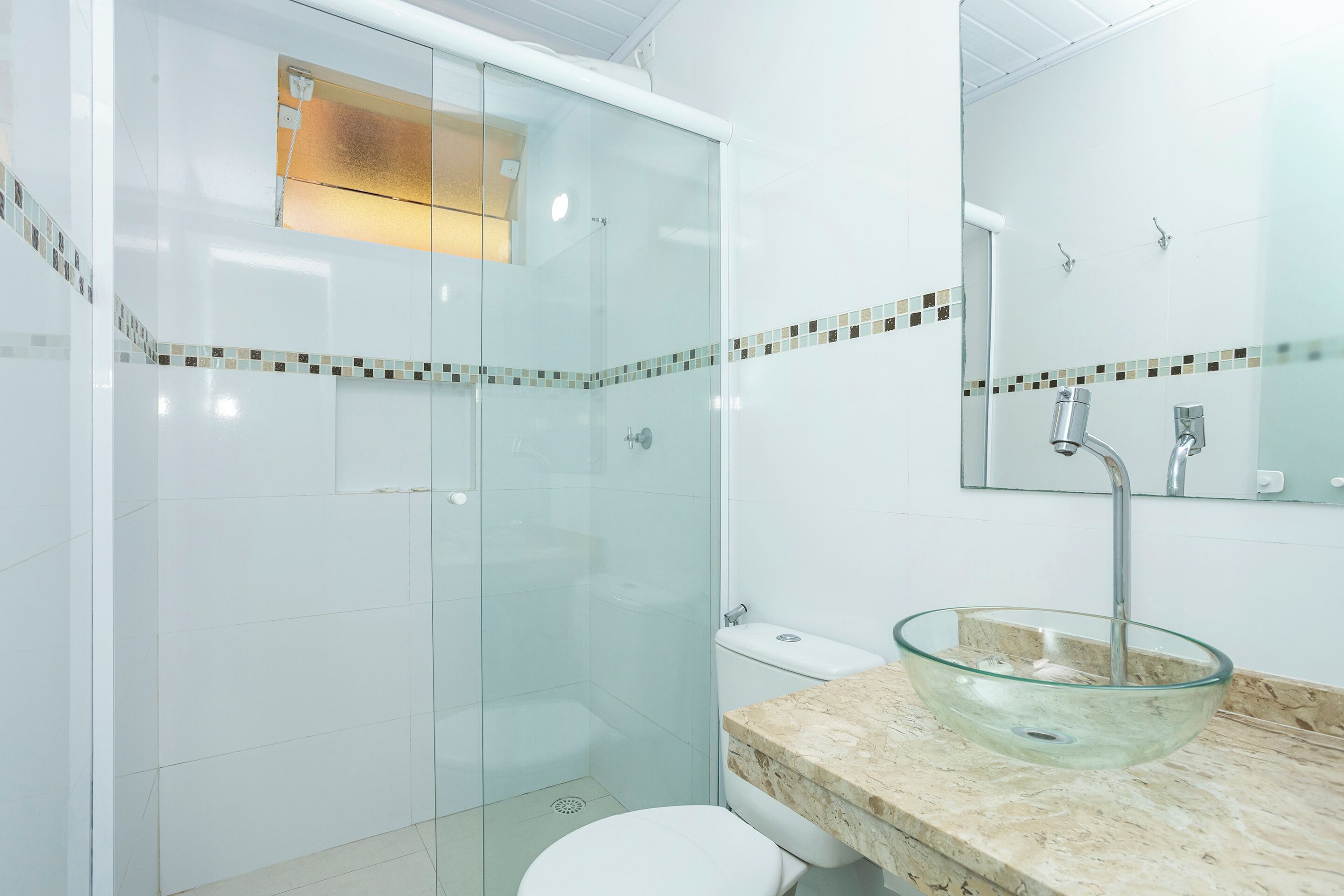 A modern bathroom with a glass-enclosed shower, a glass bowl sink, and a toilet.