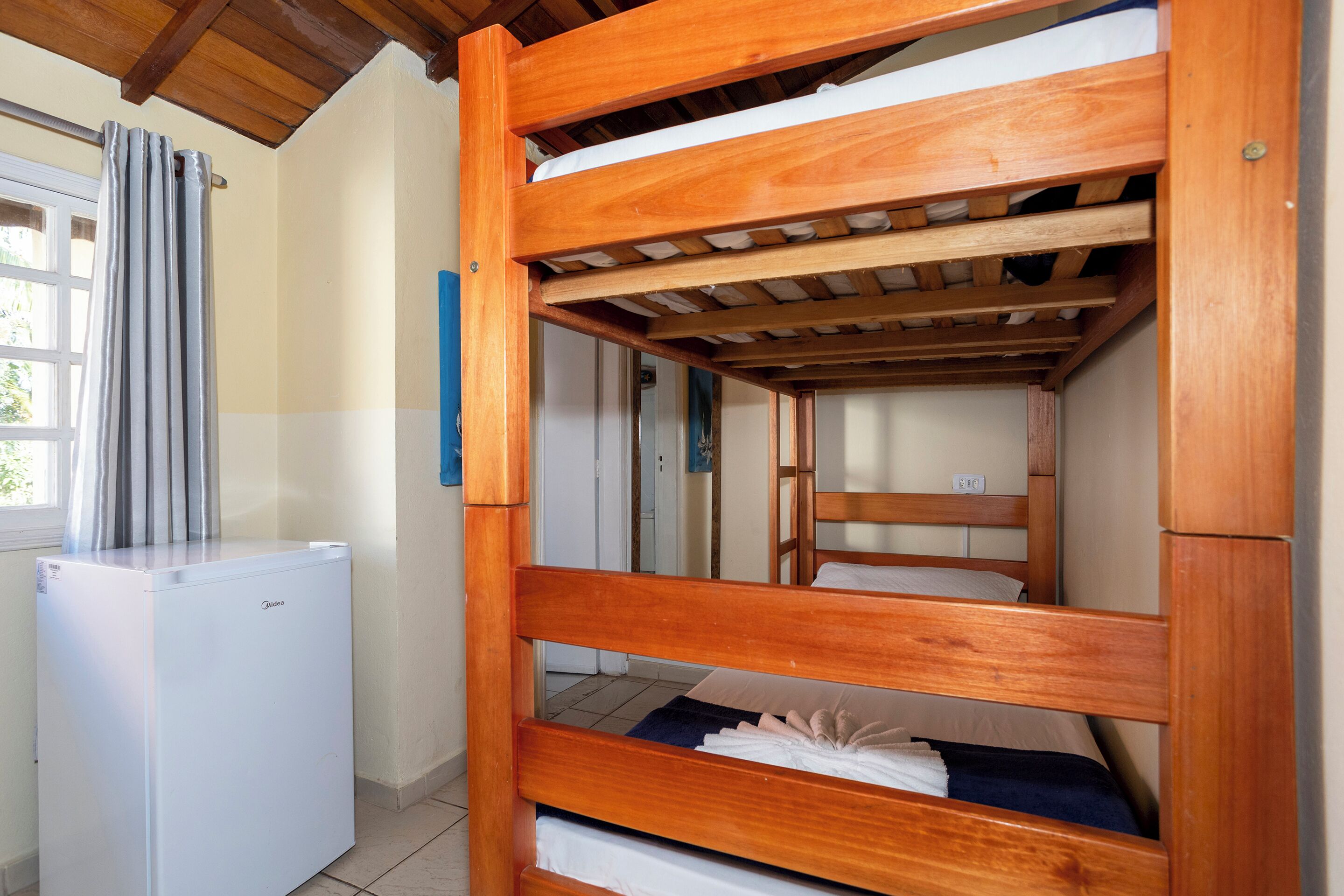 A bunk bed room with a white refrigerator and a window with curtains.