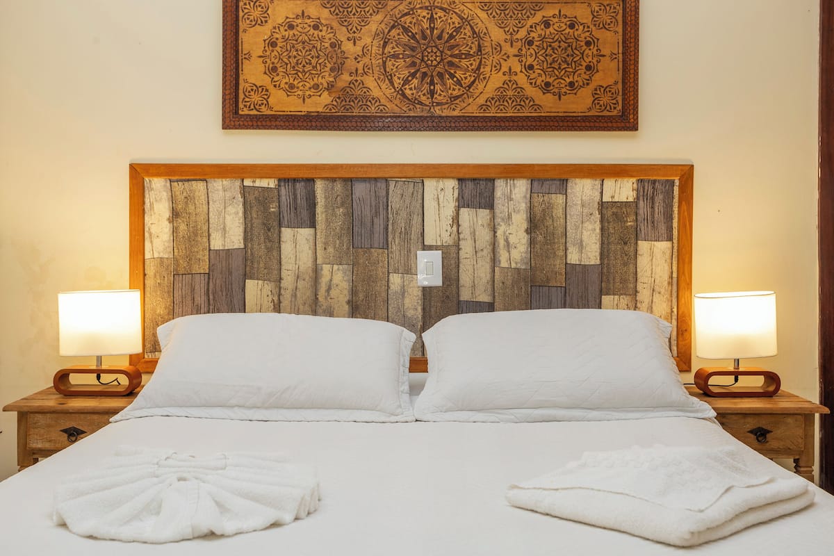 A double bed with white linens, two bedside lamps, and a wooden headboard with a geometric pattern.