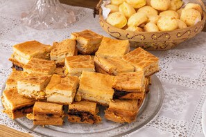 Ein Teller mit quadratischen Gebäckstücken mit goldbrauner Kruste, eine Schale mit runden, goldbraunen Gebäcken und eine Tischdecke aus Spitze.