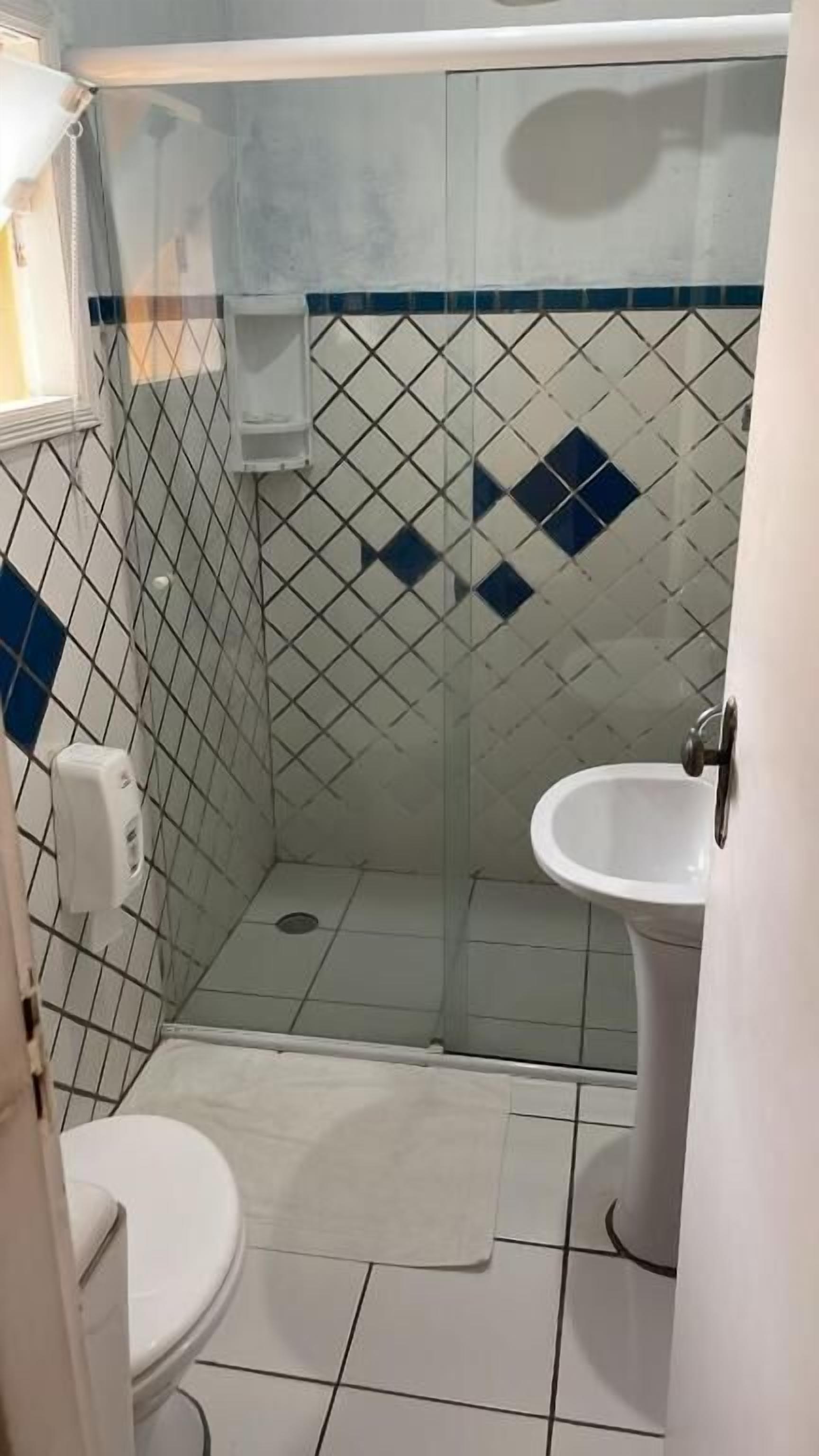 Un baño pequeño y con azulejos, con inodoro, lavamanos y zona de ducha.