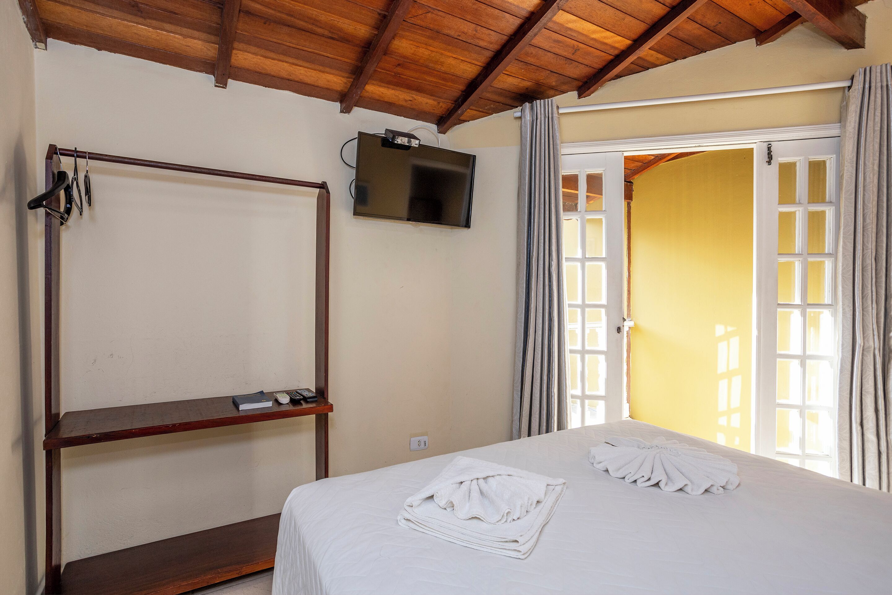 Habitación de hotel con cama, televisor montado en la pared y techo de madera.