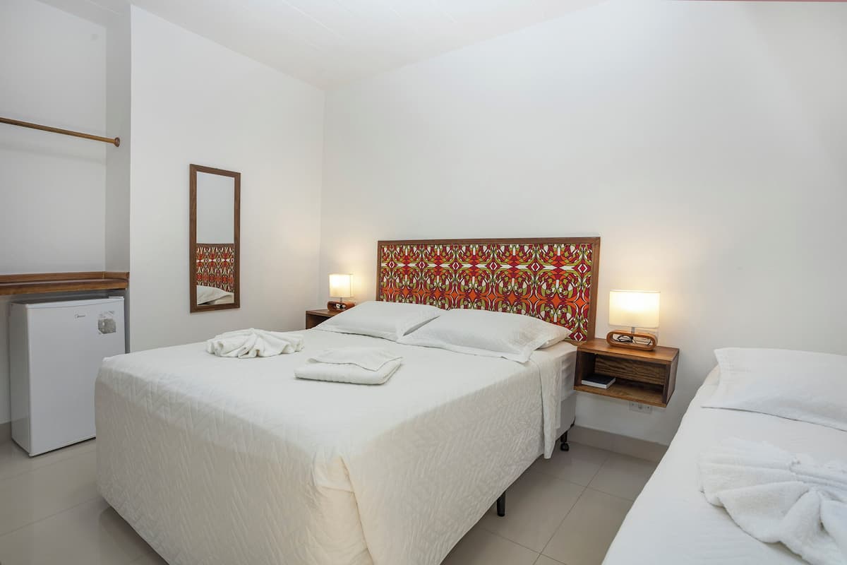 A hotel room with a bed, bedside table, lamp, and a small refrigerator.