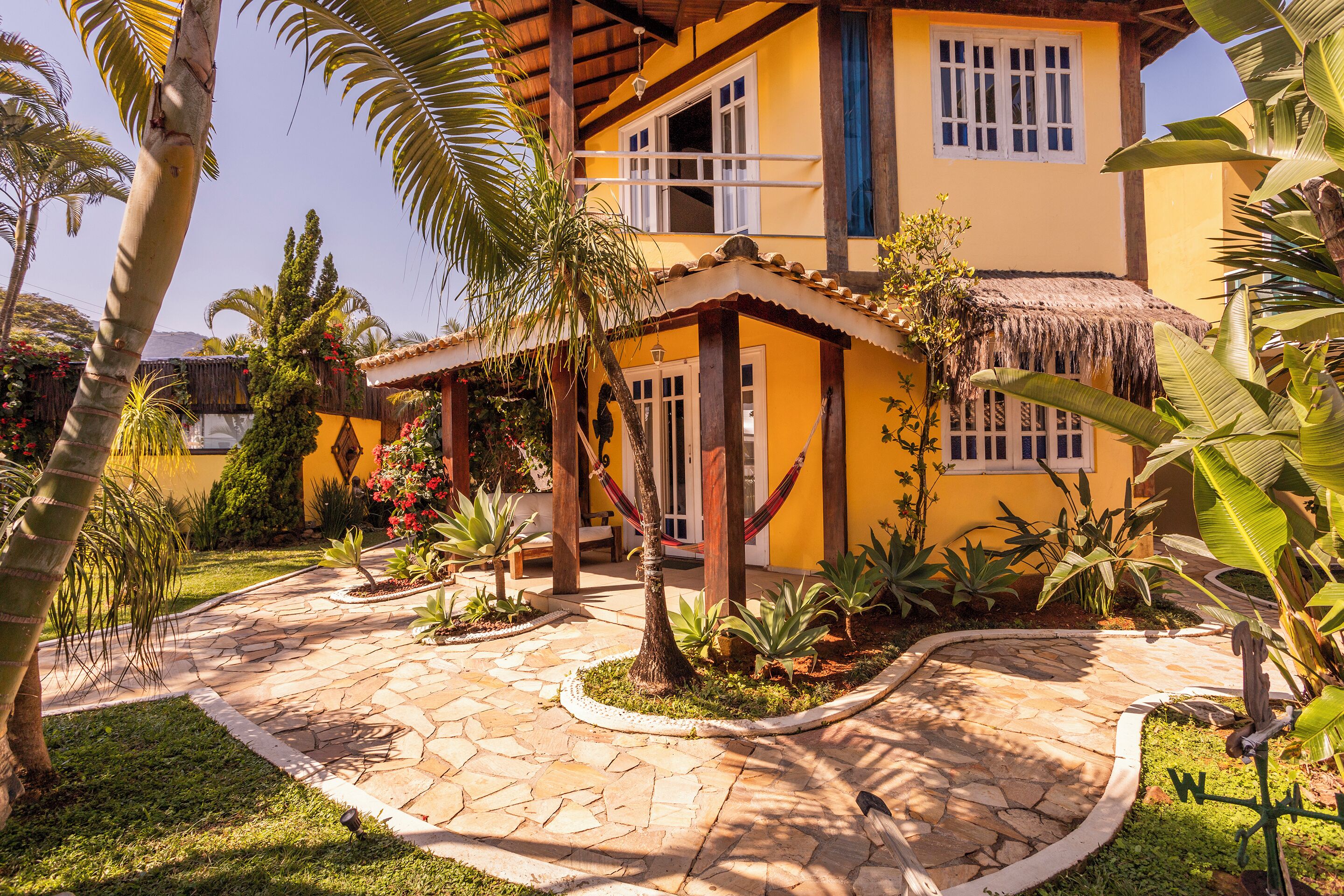 A yellow building with a thatched roof, surrounded by a stone pathway and tropical plants.
