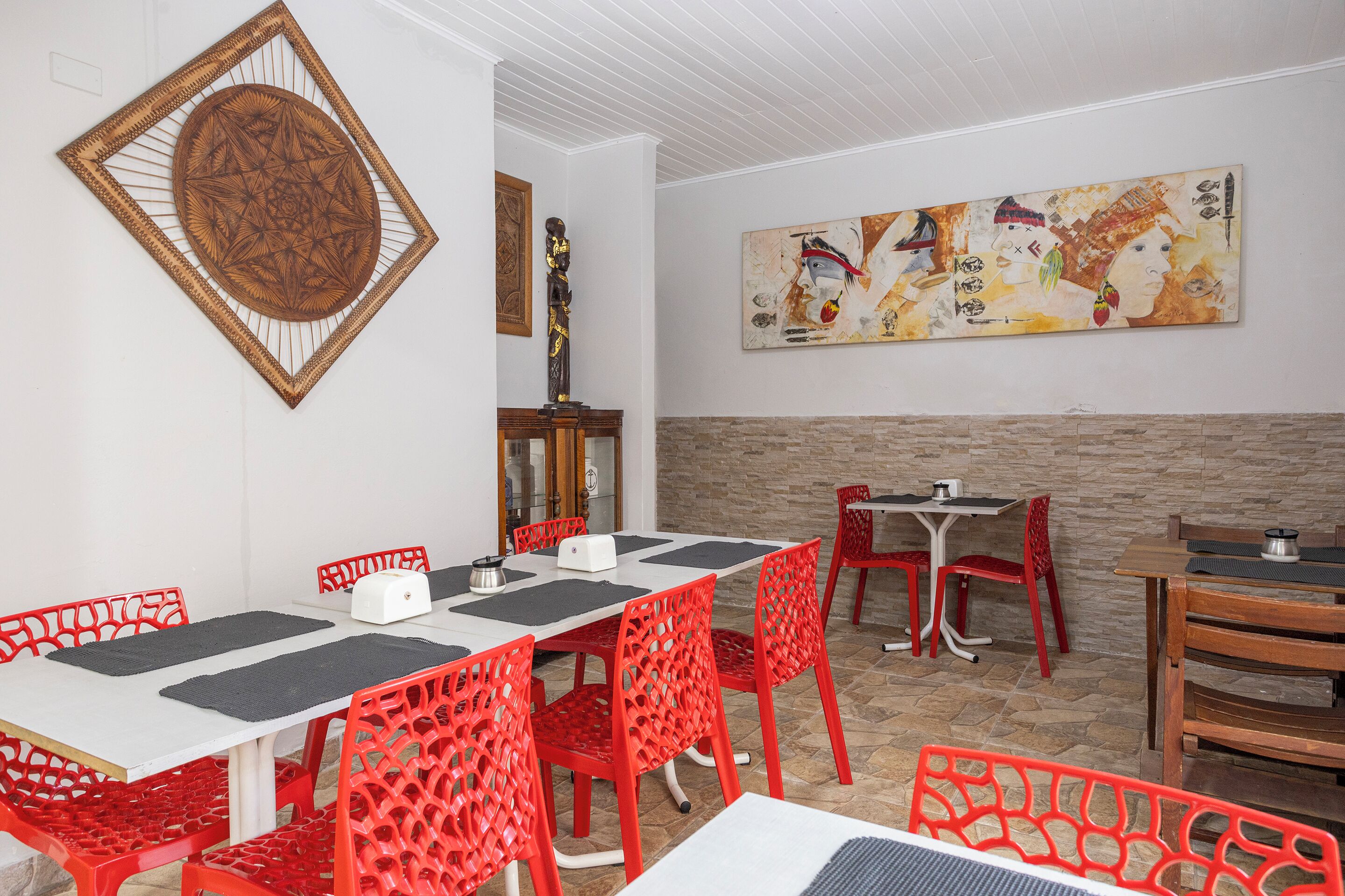 A dining area with red chairs, a white table, and a large abstract painting on the wall.