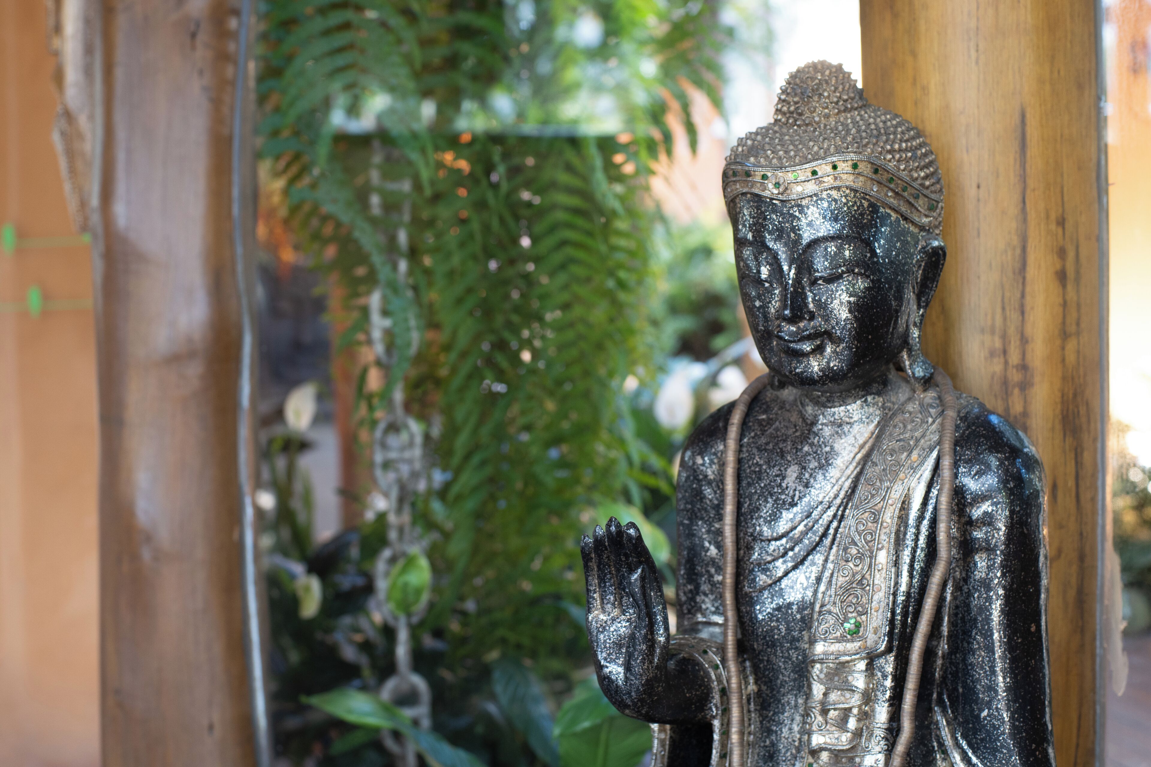 A statue of a seated figure with hands in a prayer position, surrounded by greenery.